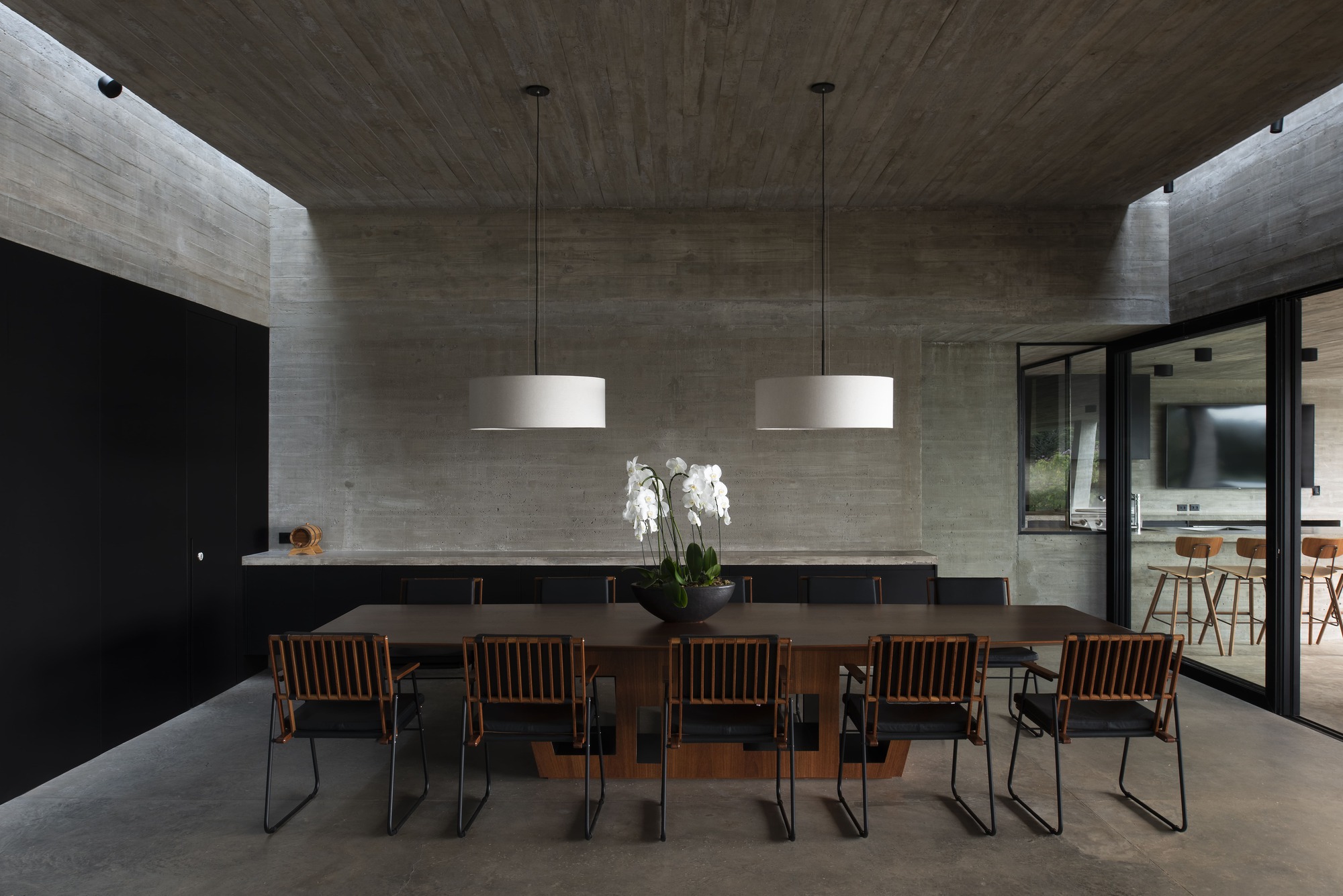 Dining room with boardmarked concrete ceiling and walls flanking a long table under pendant lights