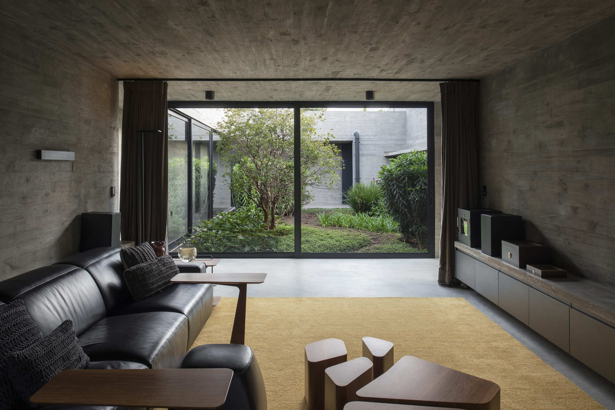 Living room with board-formed concrete walls and glazed doors revealing a courtyard garden with trees
