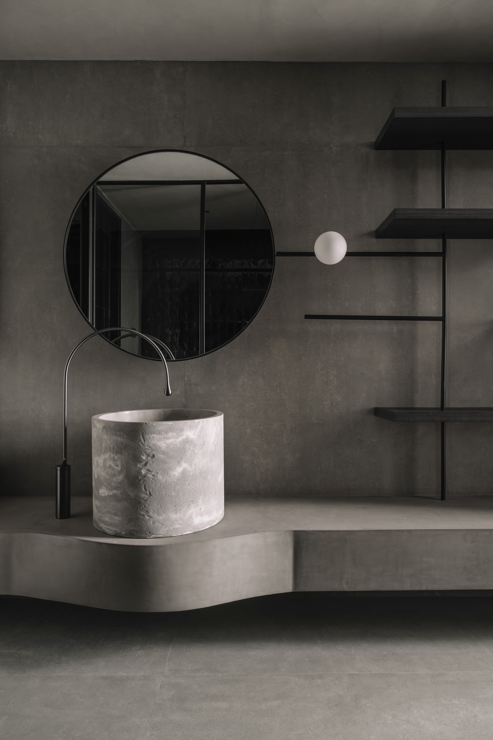 Bathroom vanity detail with cylindrical white stone basin and circular mirror against concrete wall