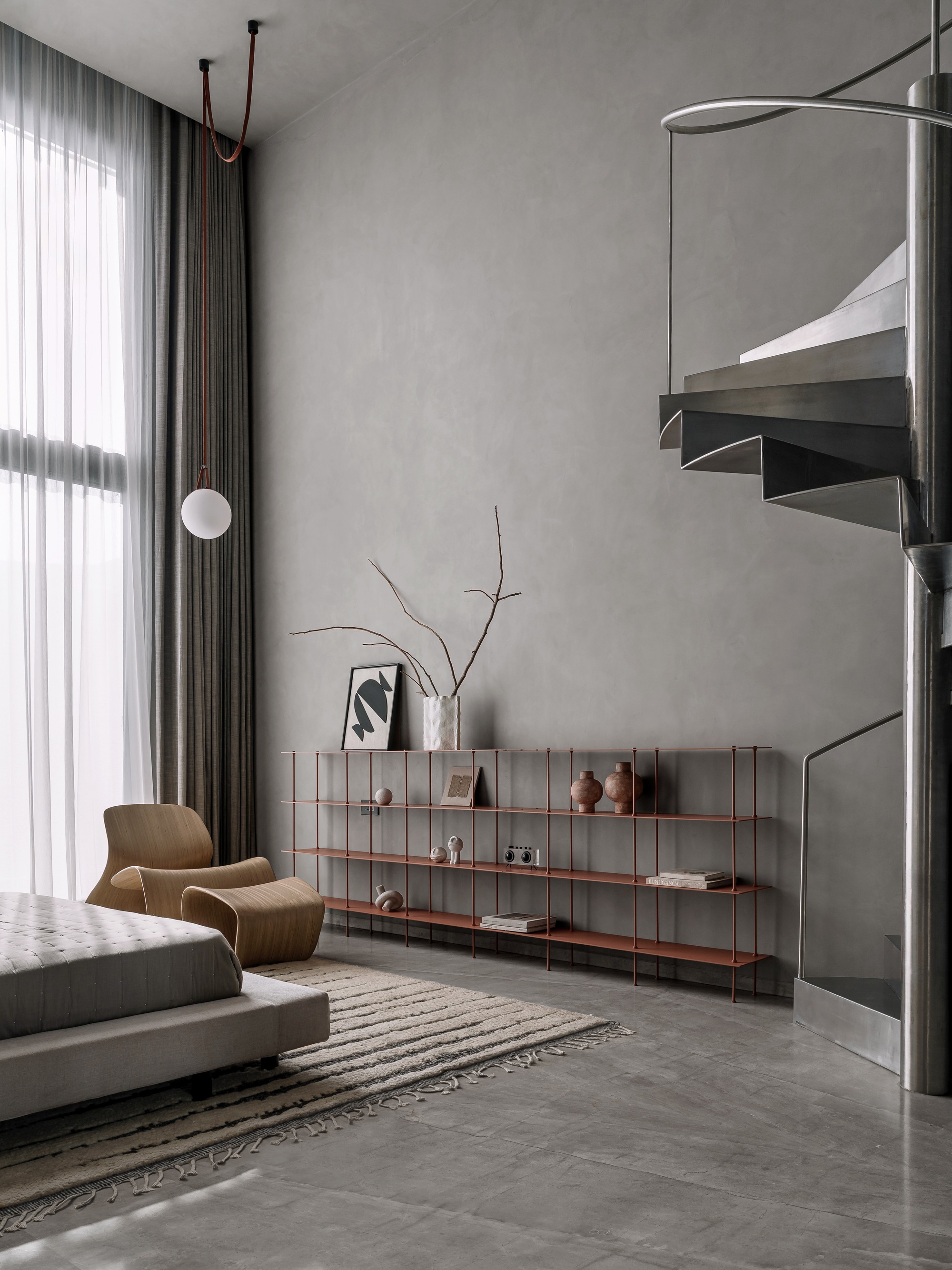 Steel spiral staircase with floating treads beside low shelving unit and grey curtain wall