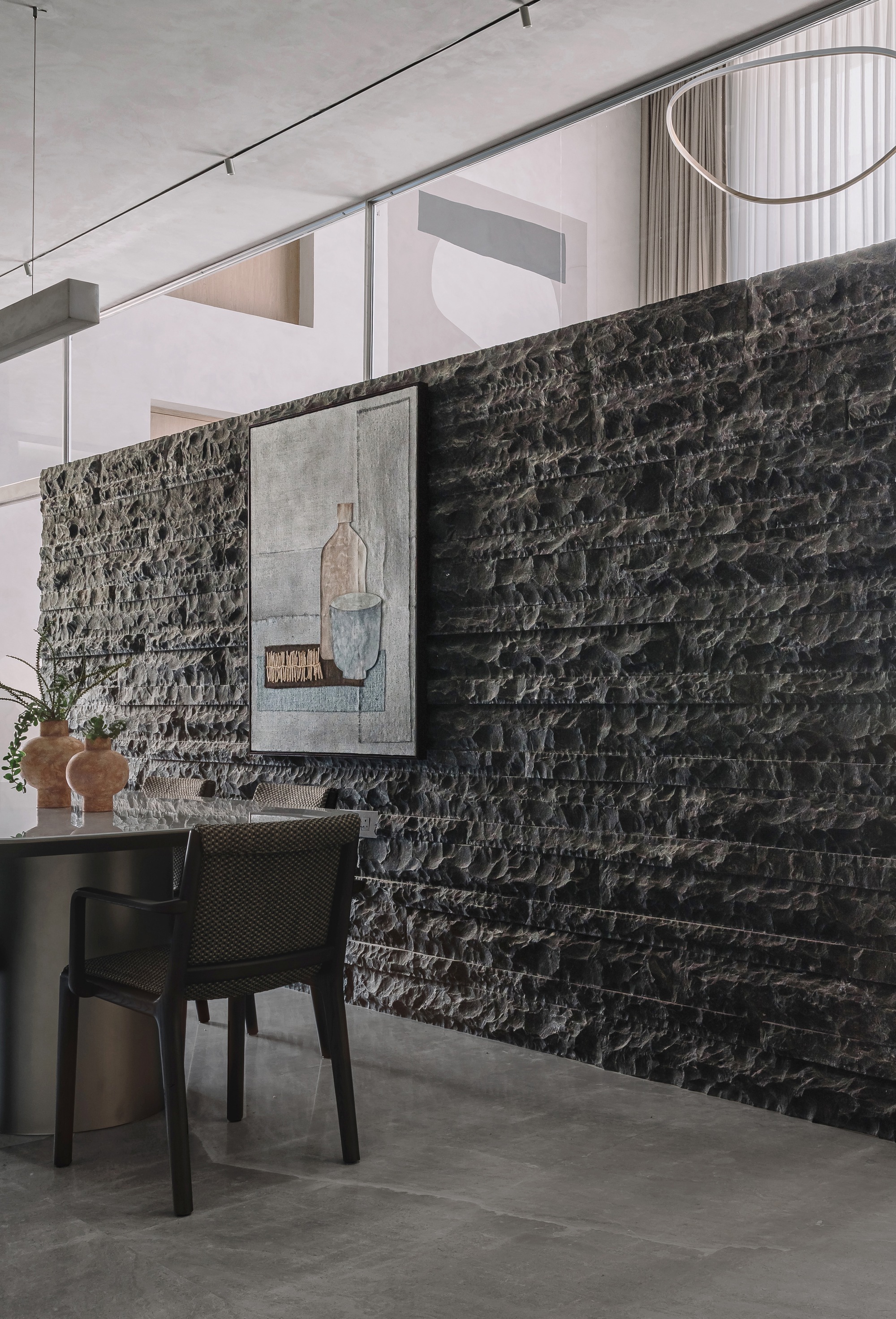Dark split-face stone wall with framed artwork and dining table in soft daylight
