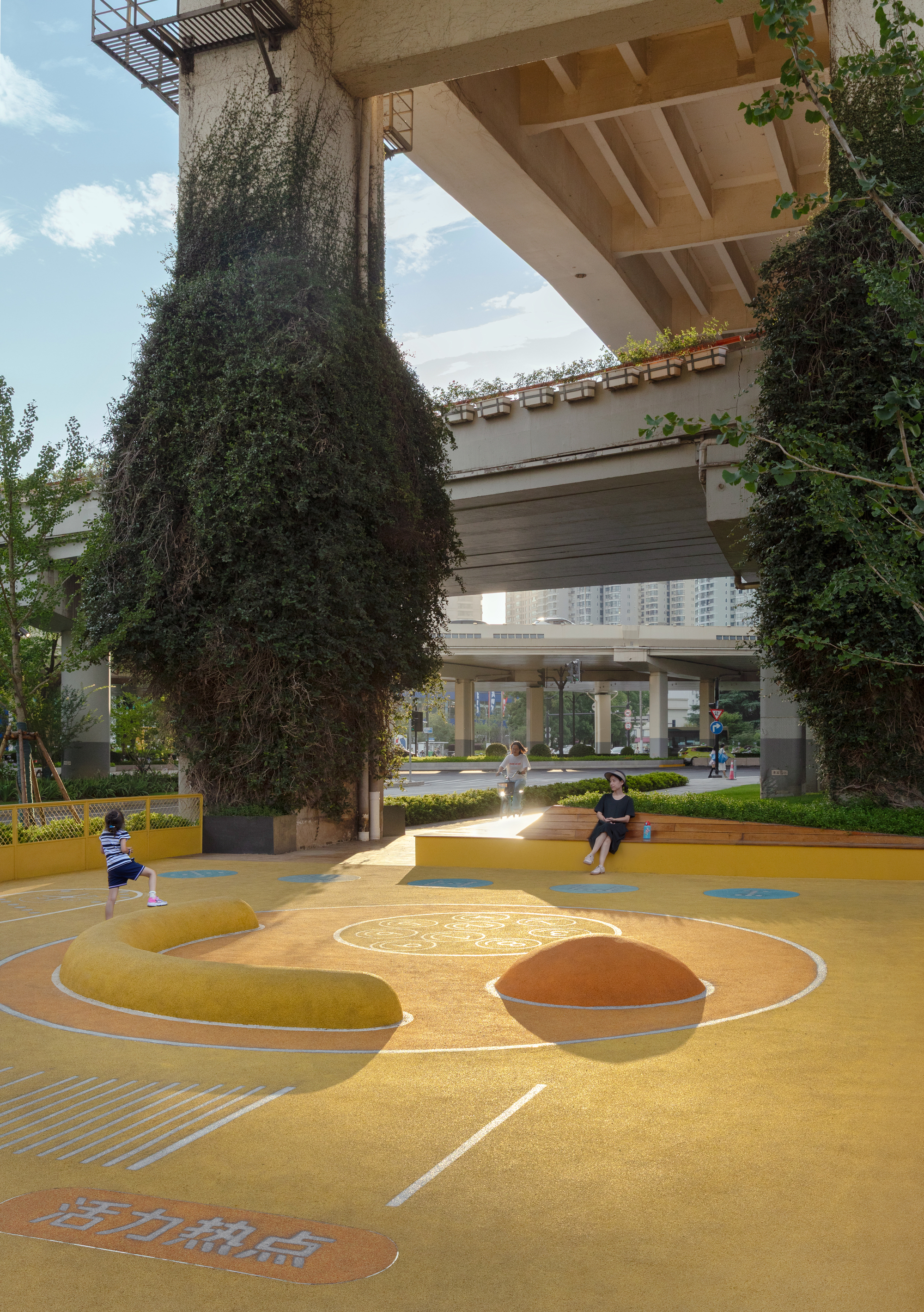 Yellow play court with raised circular mounds beneath the planted viaduct columns in afternoon sunlight