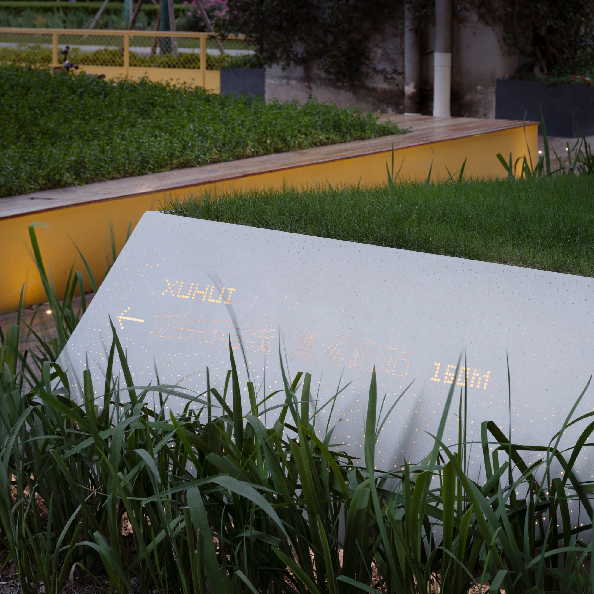 Perforated white panel with interior lighting surrounded by tall grasses at dusk