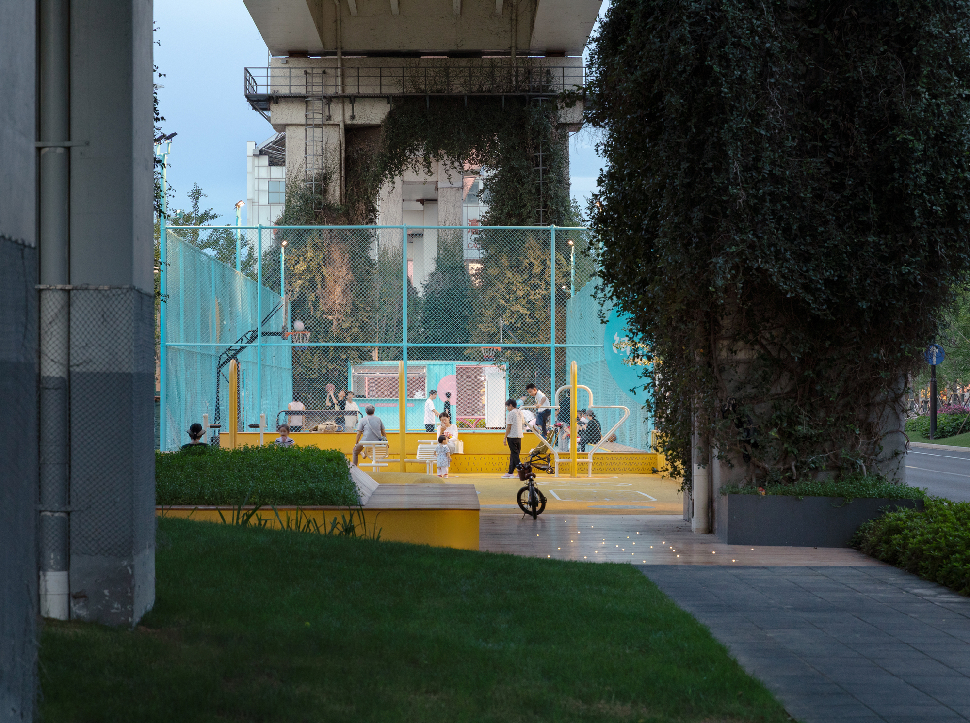 Basketball court under an elevated concrete structure with people playing at twilight