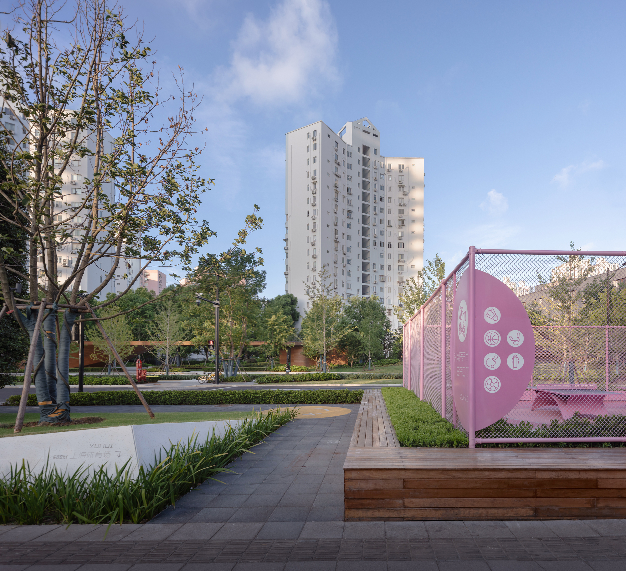 Pink mesh pavilion with graphic motifs beside paved pathways and planted beds in afternoon light