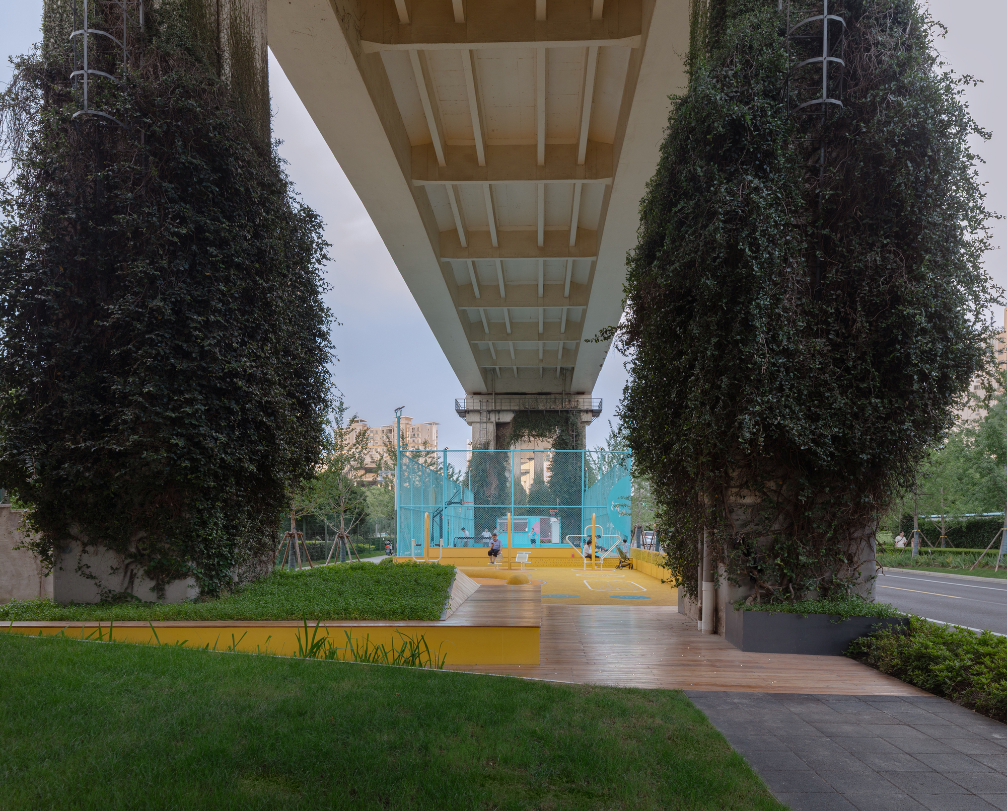 Underside of concrete bridge deck framing lawn and timber pathway between vine-covered support columns at dusk