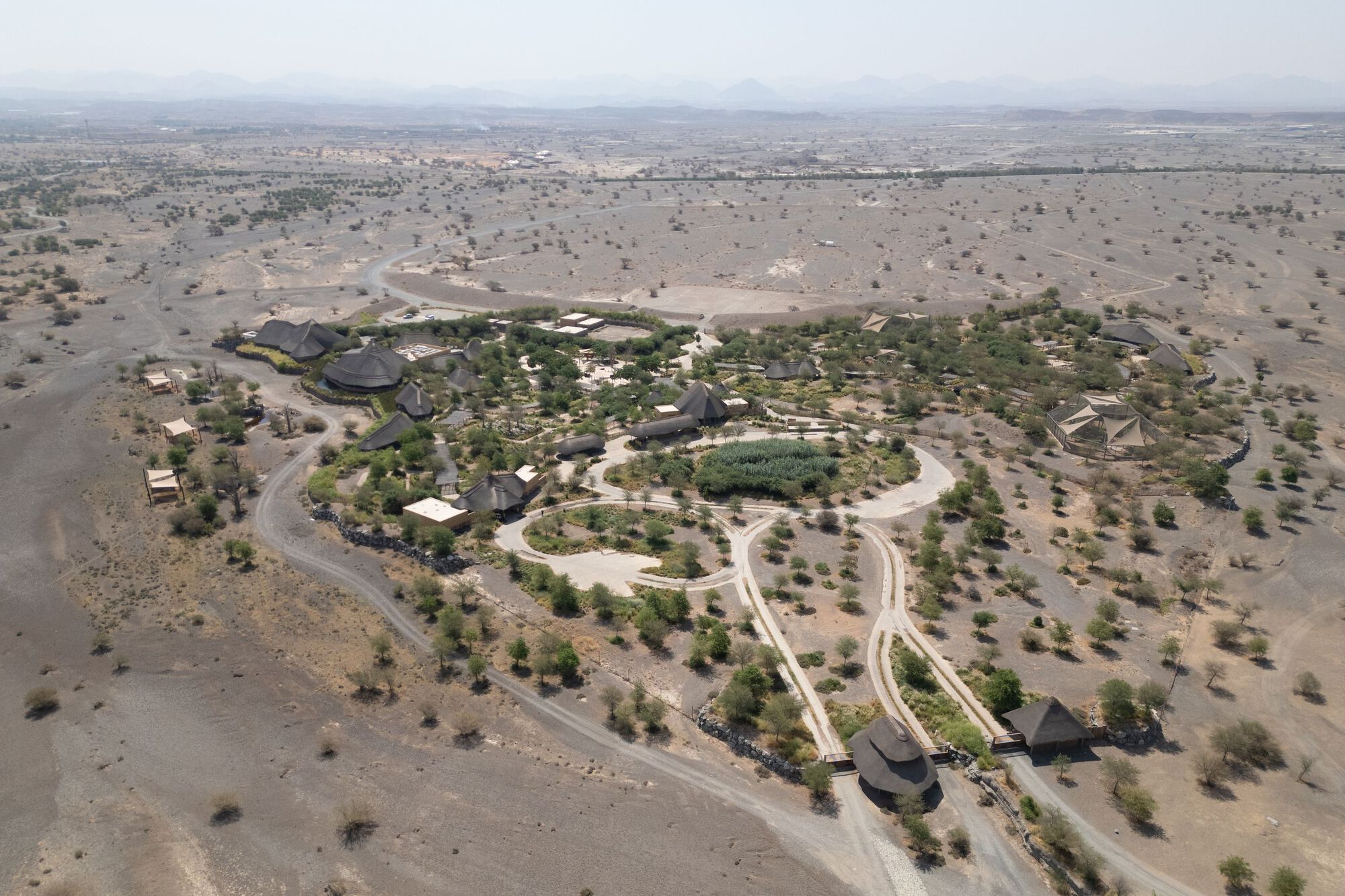 Aerial view of the compound with thatched structures clustered within landscaped grounds in arid terrain