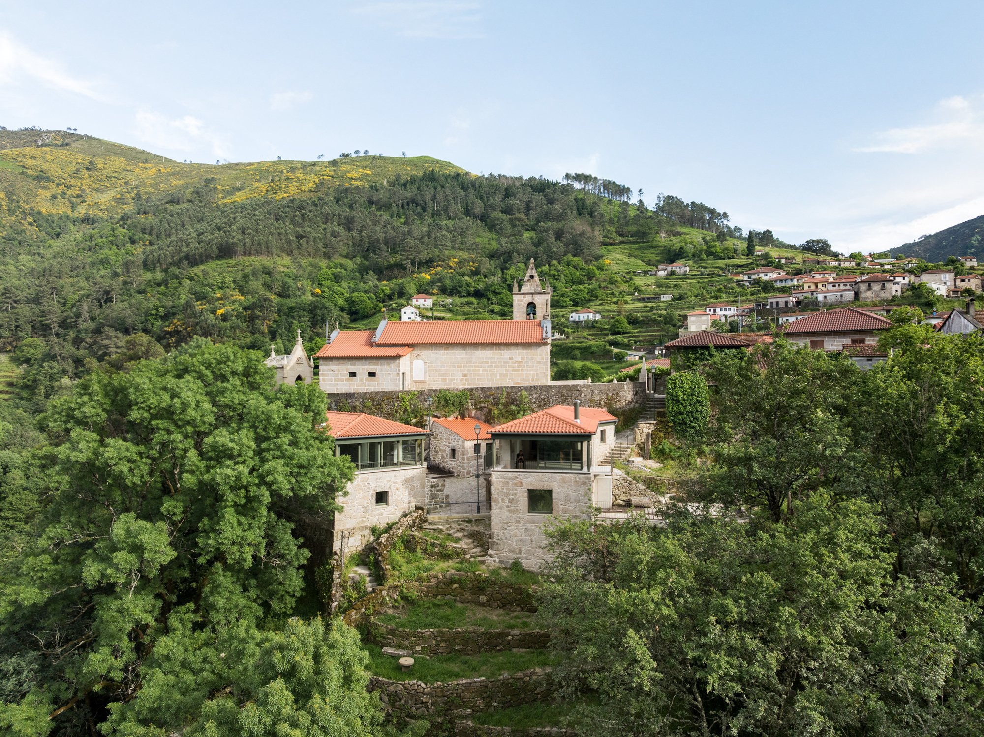 Cluster of stone houses with terracotta roofs and church bell tower set within terraced green hillsides