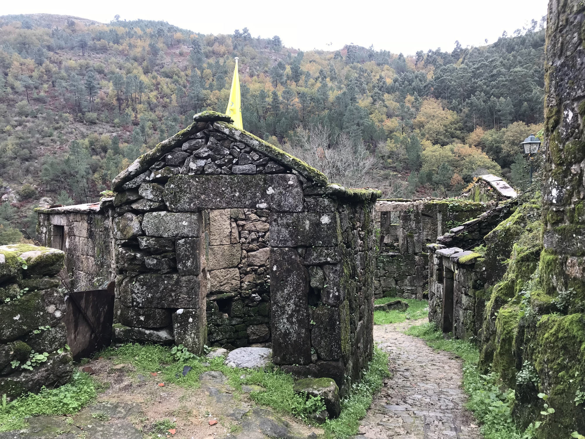 Ruins of stone structures with moss-covered walls along a cobblestone path in the hillside
