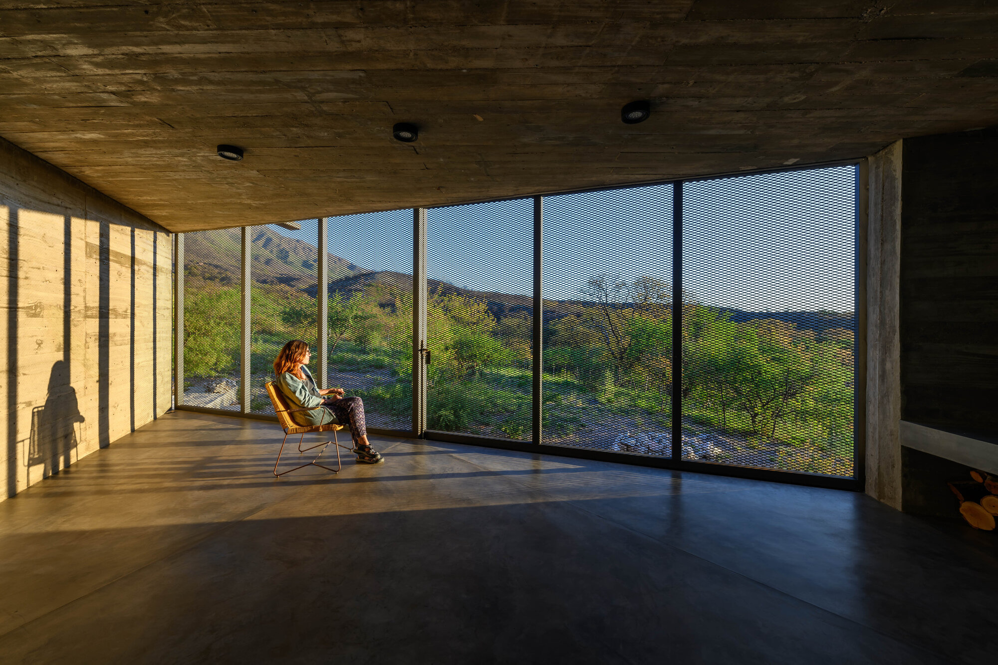Interior room with floor-to-ceiling glazing overlooking mountainous landscape, timber ceiling overhead with a seated figure