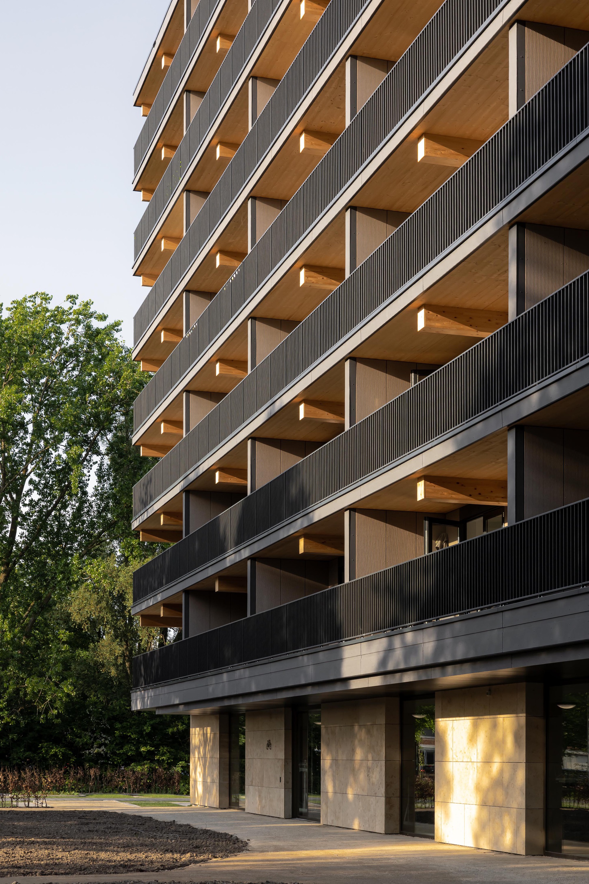 Stacked timber-lined balconies with vertical metal screening and concrete columns at ground level