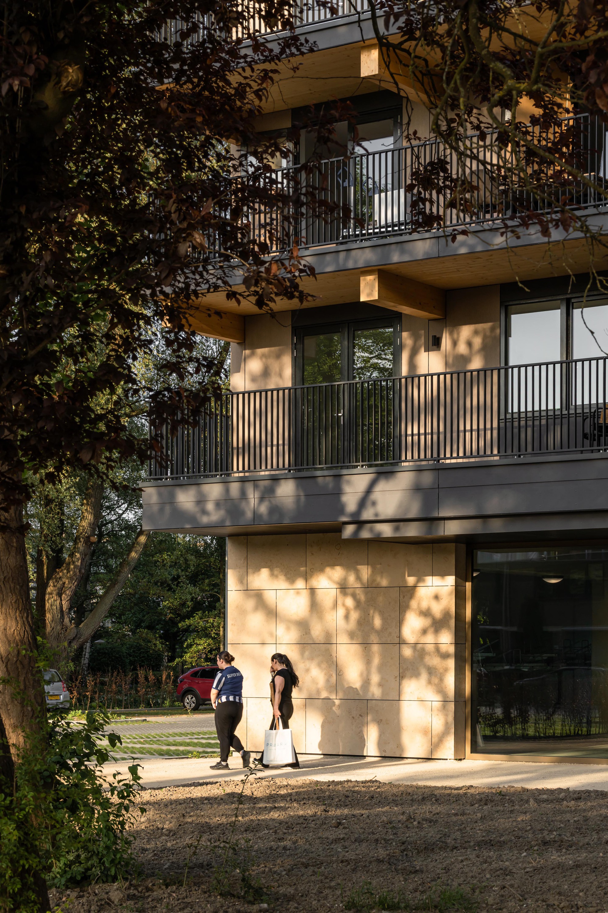 Timber-clad balconies casting dappled shadows with two pedestrians near the entrance at sunset