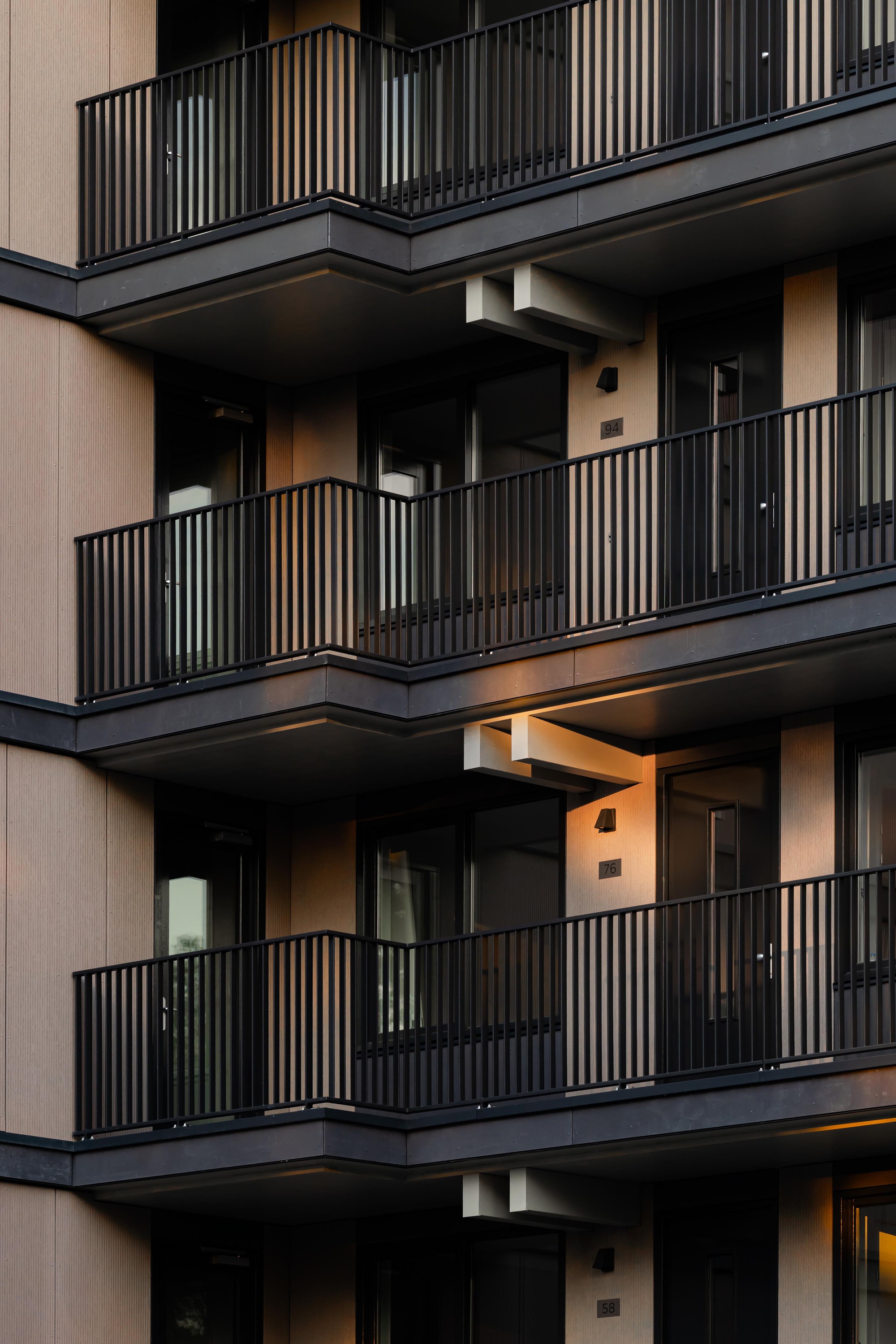 Stacked balconies with vertical metal railings and recessed openings illuminated at twilight