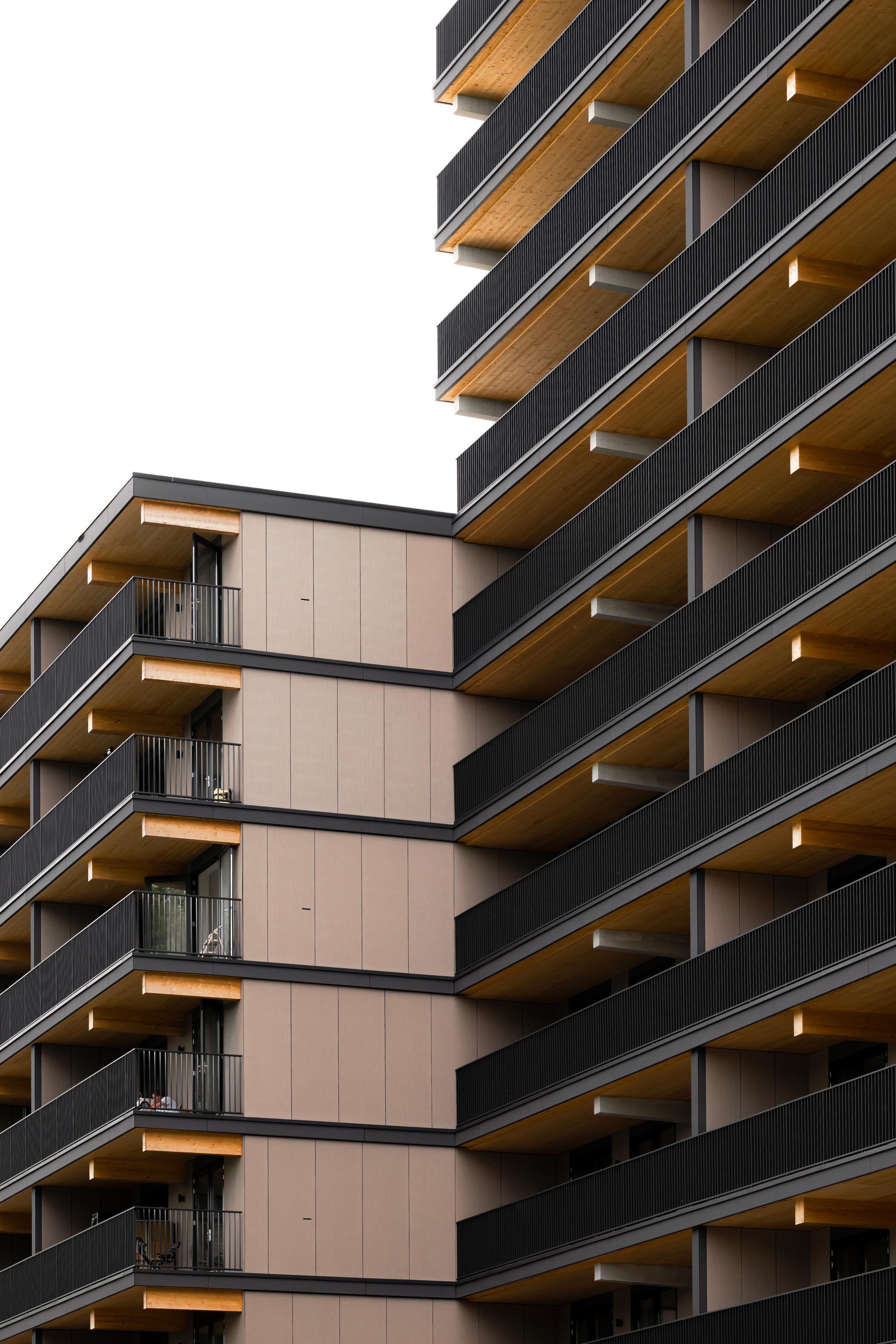 Close-up of stacked balconies with timber soffits and dark metal railings against an overcast sky