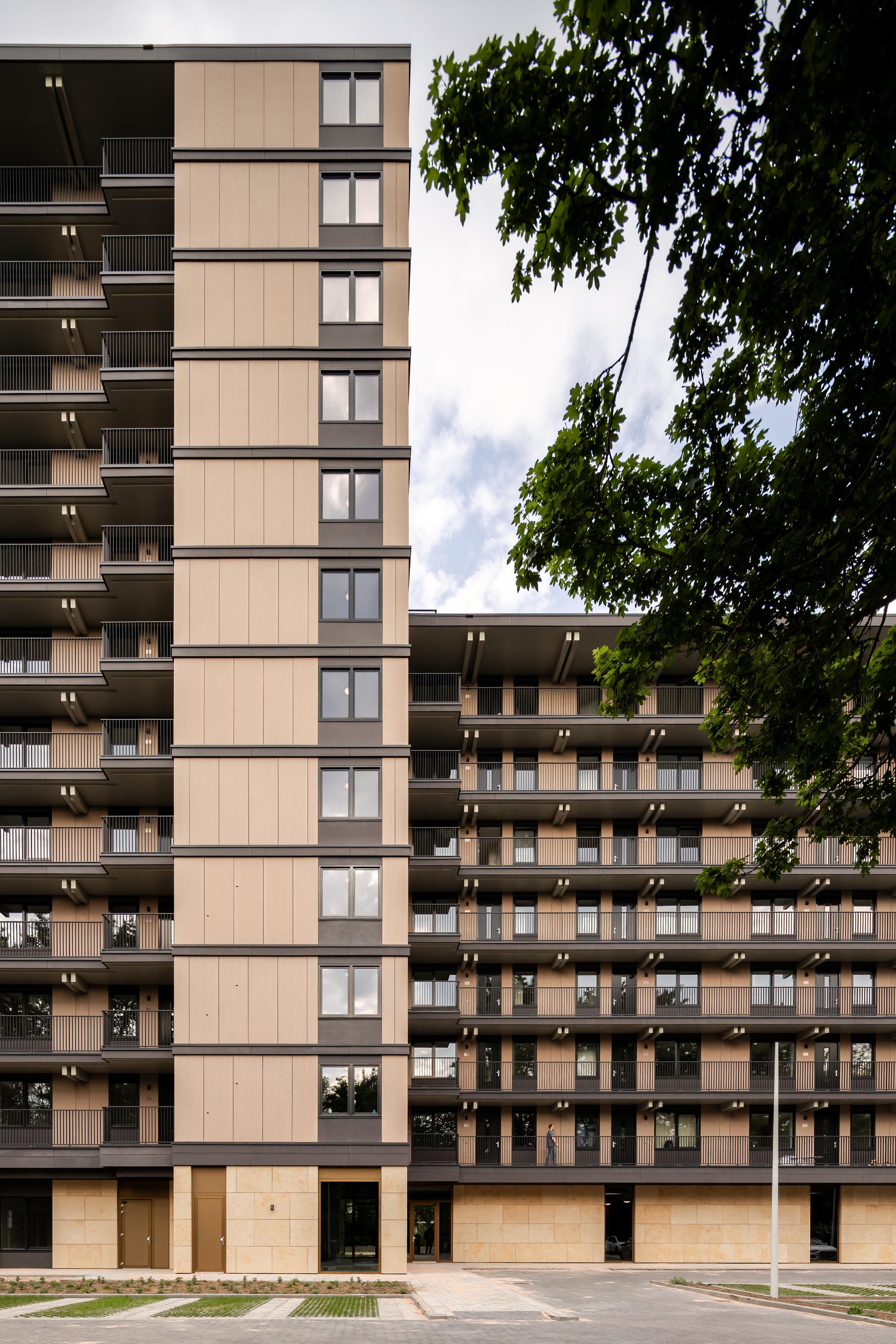 Street view of two residential towers with vertical panel cladding framed by deciduous trees