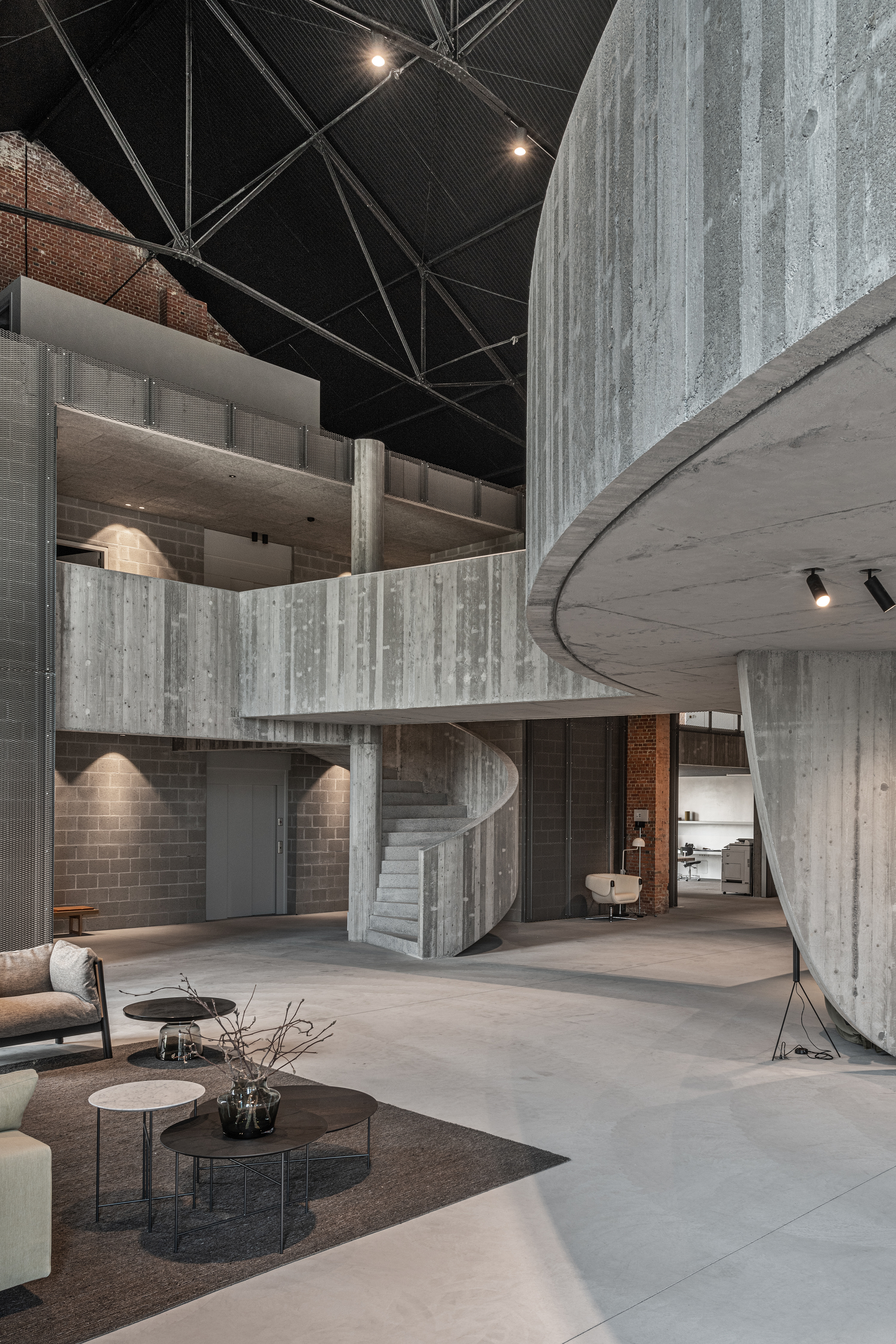 Double-height interior space with board-formed concrete stair and curved mezzanine under black metal ceiling
