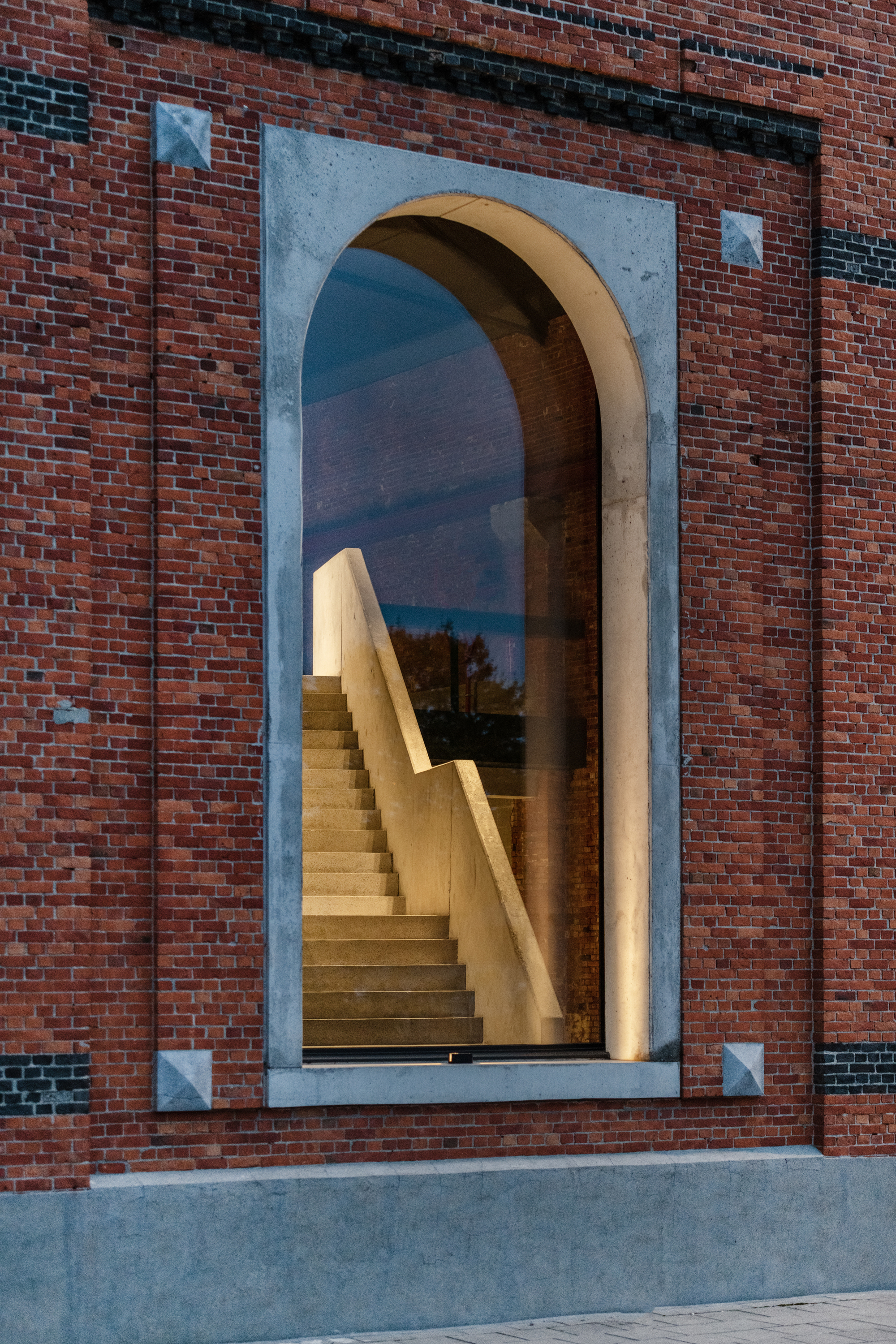Arched window with pale concrete surround frames timber staircase behind glazing