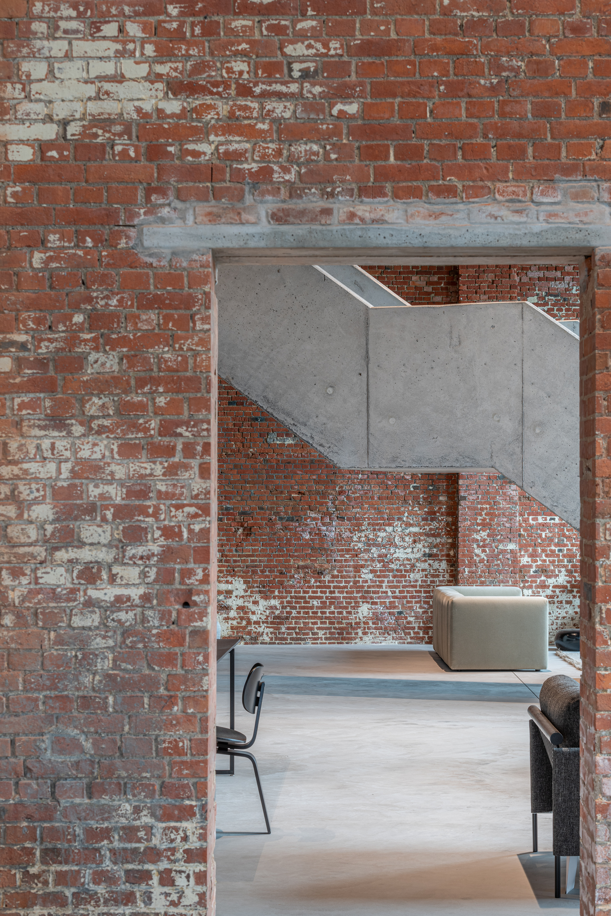 Exposed brick doorway framed by a cantilevered concrete beam above a seating area