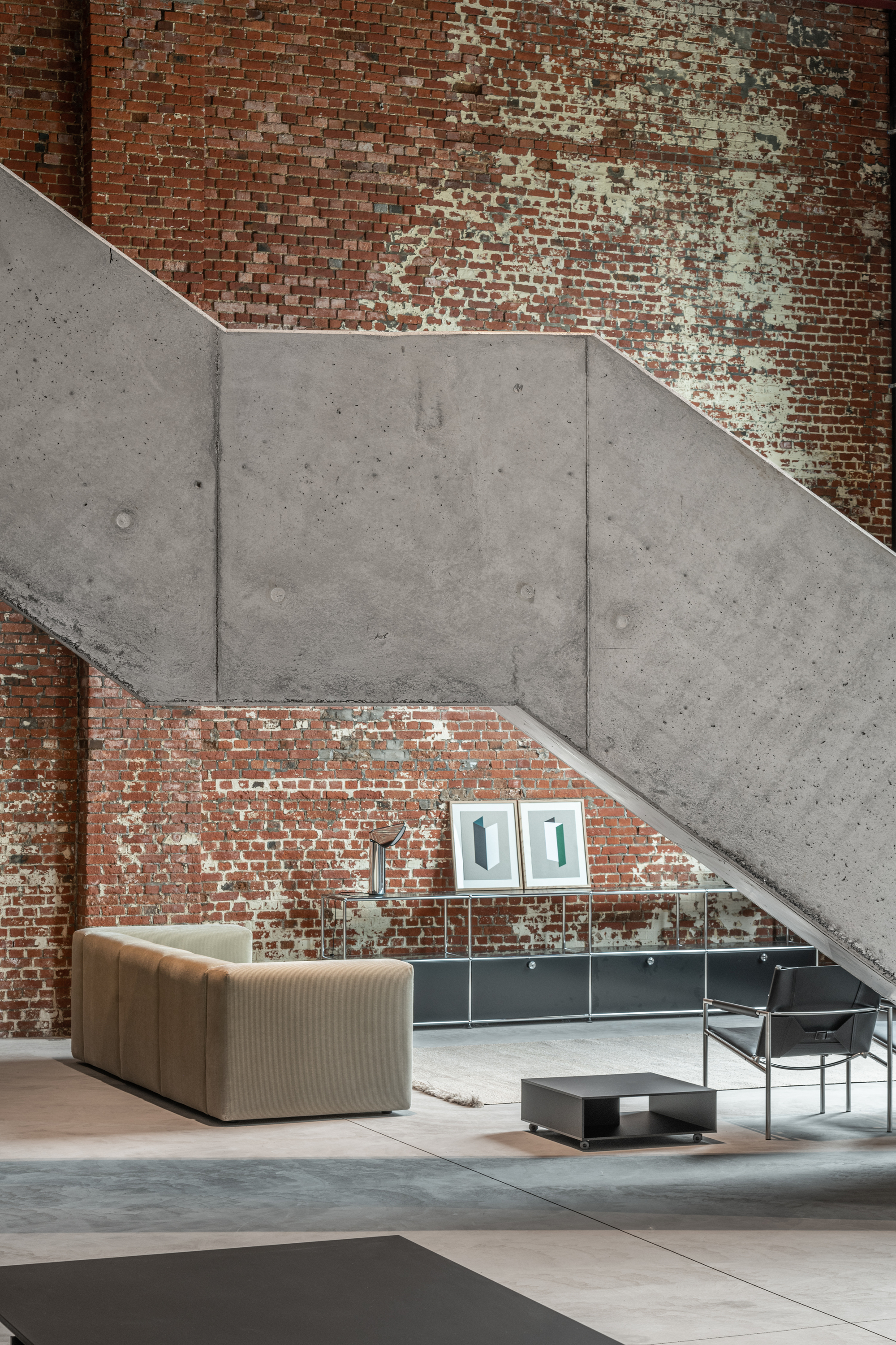 Angular concrete stair soffit cutting across weathered red brick wall with seating below