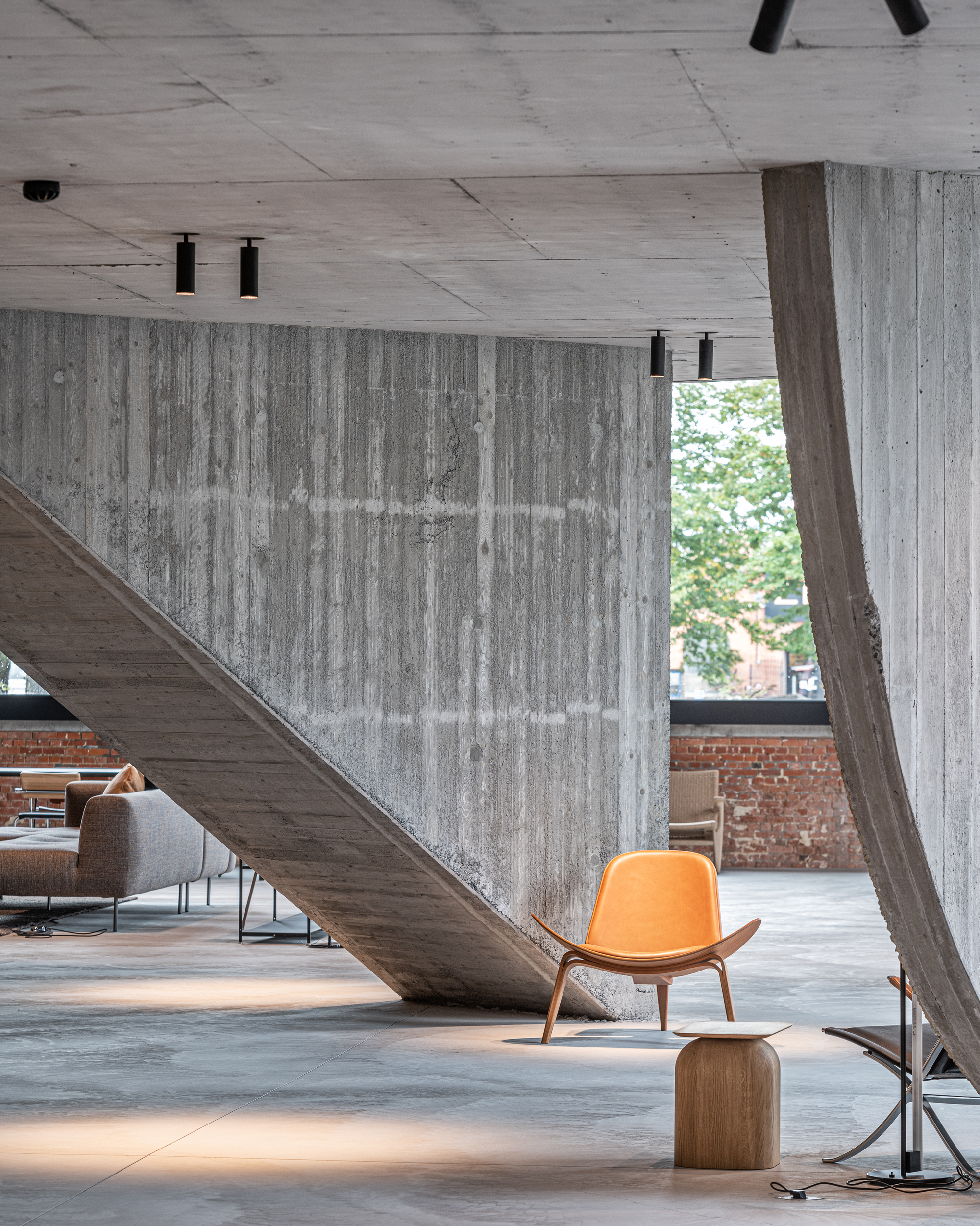 Board-formed concrete stair underside with orange upholstered chair and angled concrete column