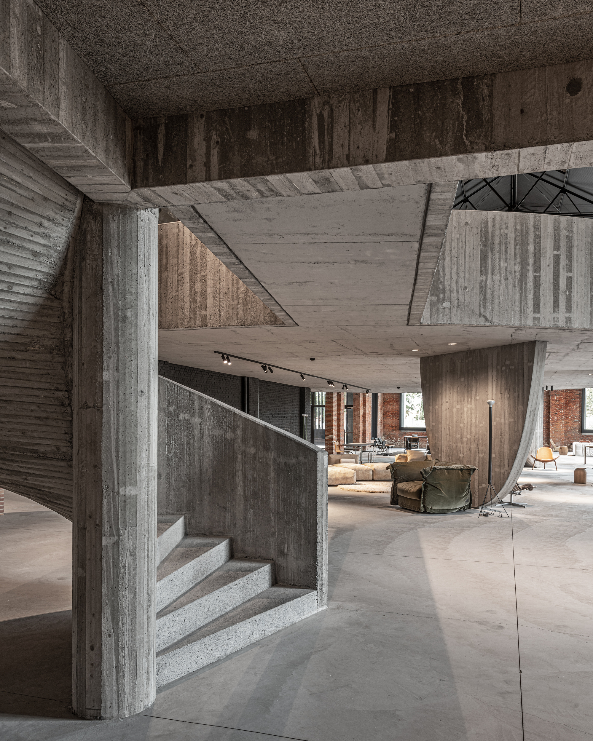 Concrete staircase wrapping around angular column beneath cantilevered upper floor slabs