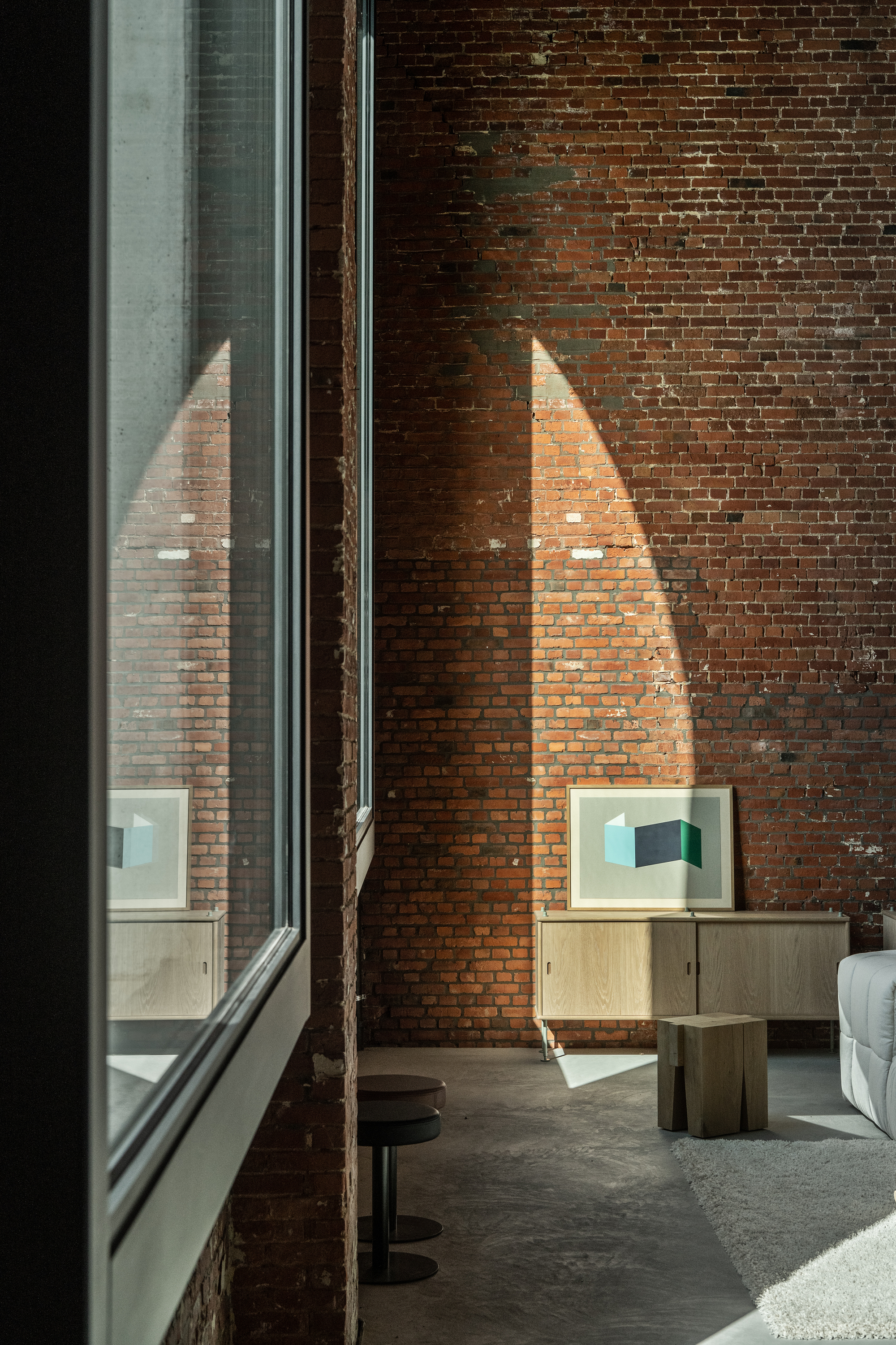 Interior view of exposed brick wall with tall window and triangular patch of afternoon sunlight