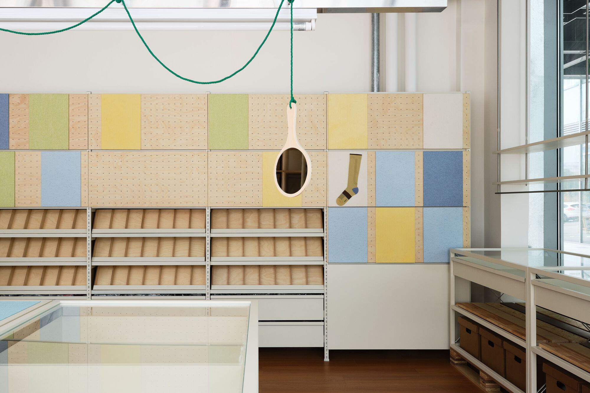 Modular storage wall with pastel pegboard panels, timber shelving units and pendant lights on green cables