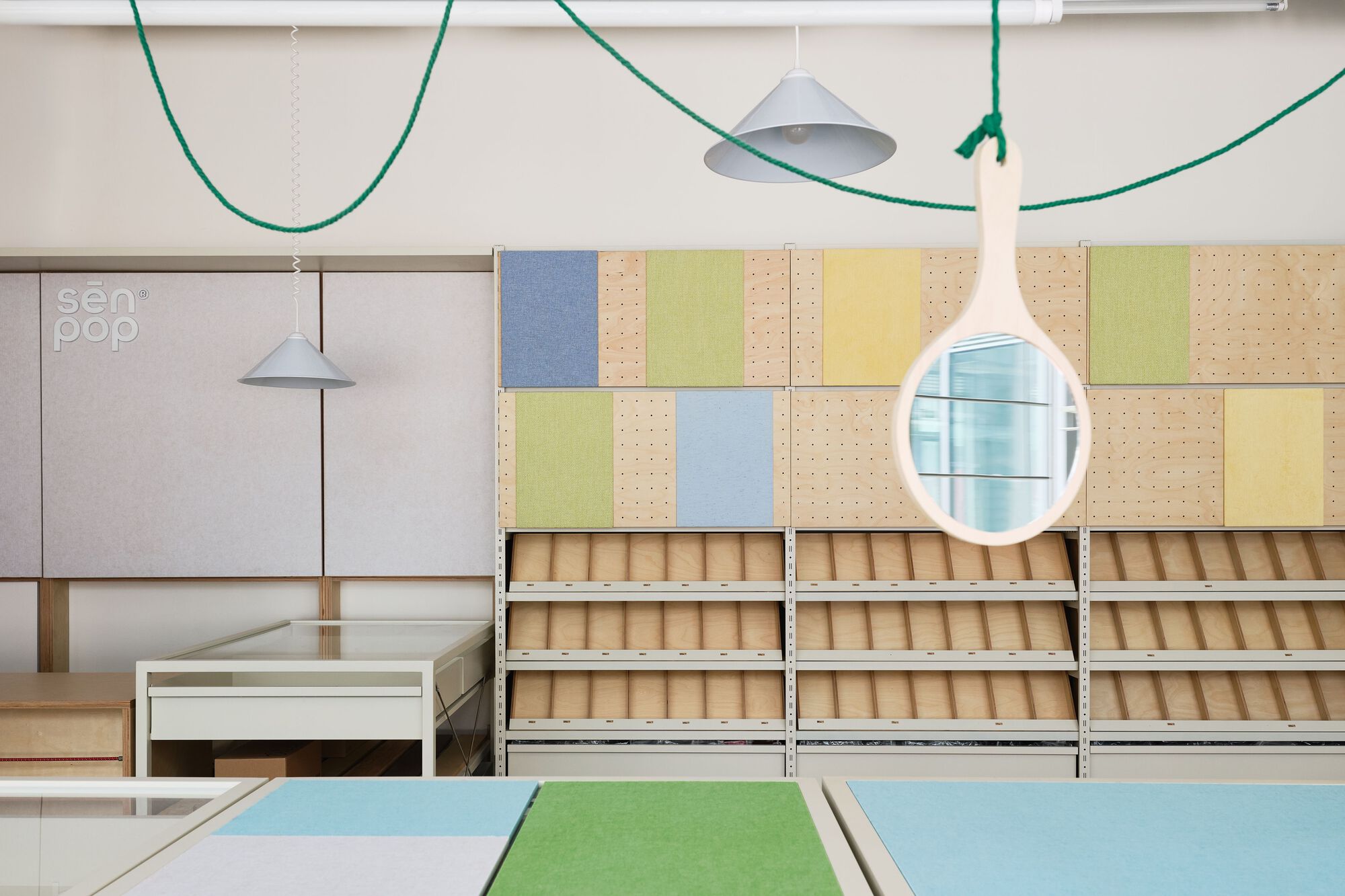 Display wall with plywood shelving units and multicolored perforated panels beneath pendant lights and green cable