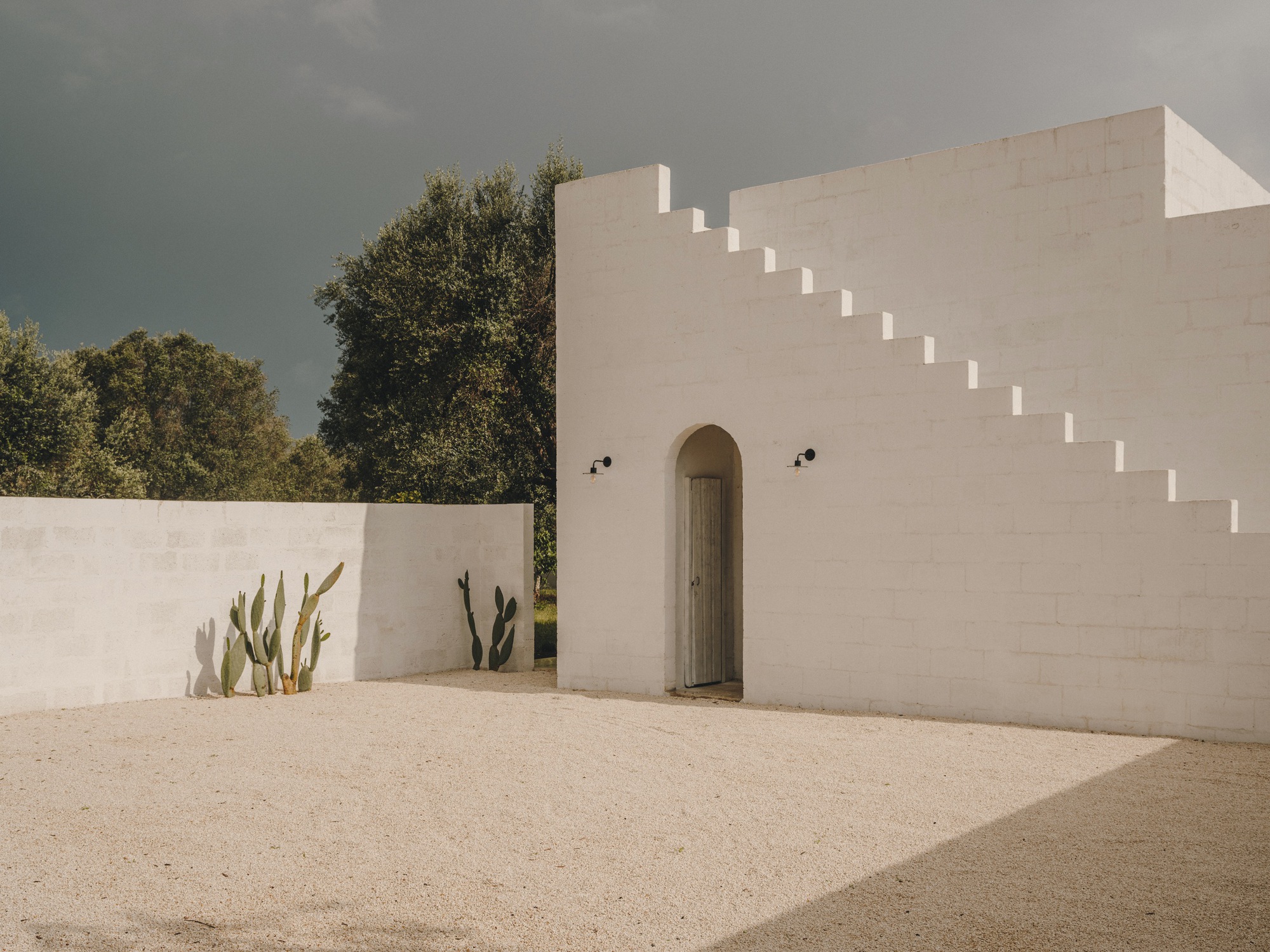 White rendered courtyard wall with stepped parapet and arched doorway flanked by cacti