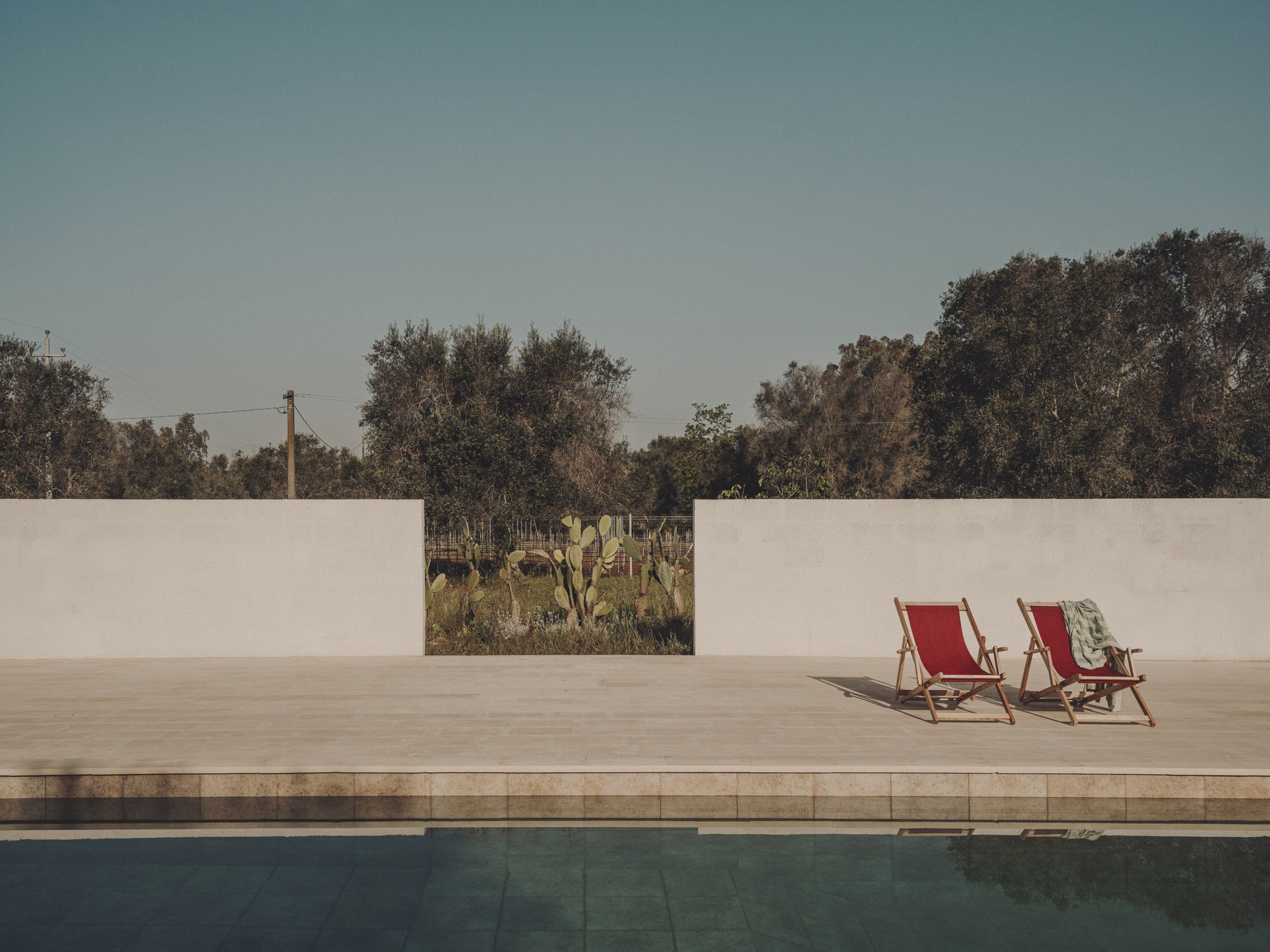 Poolside terrace with framed opening in the wall revealing cacti and trees beyond