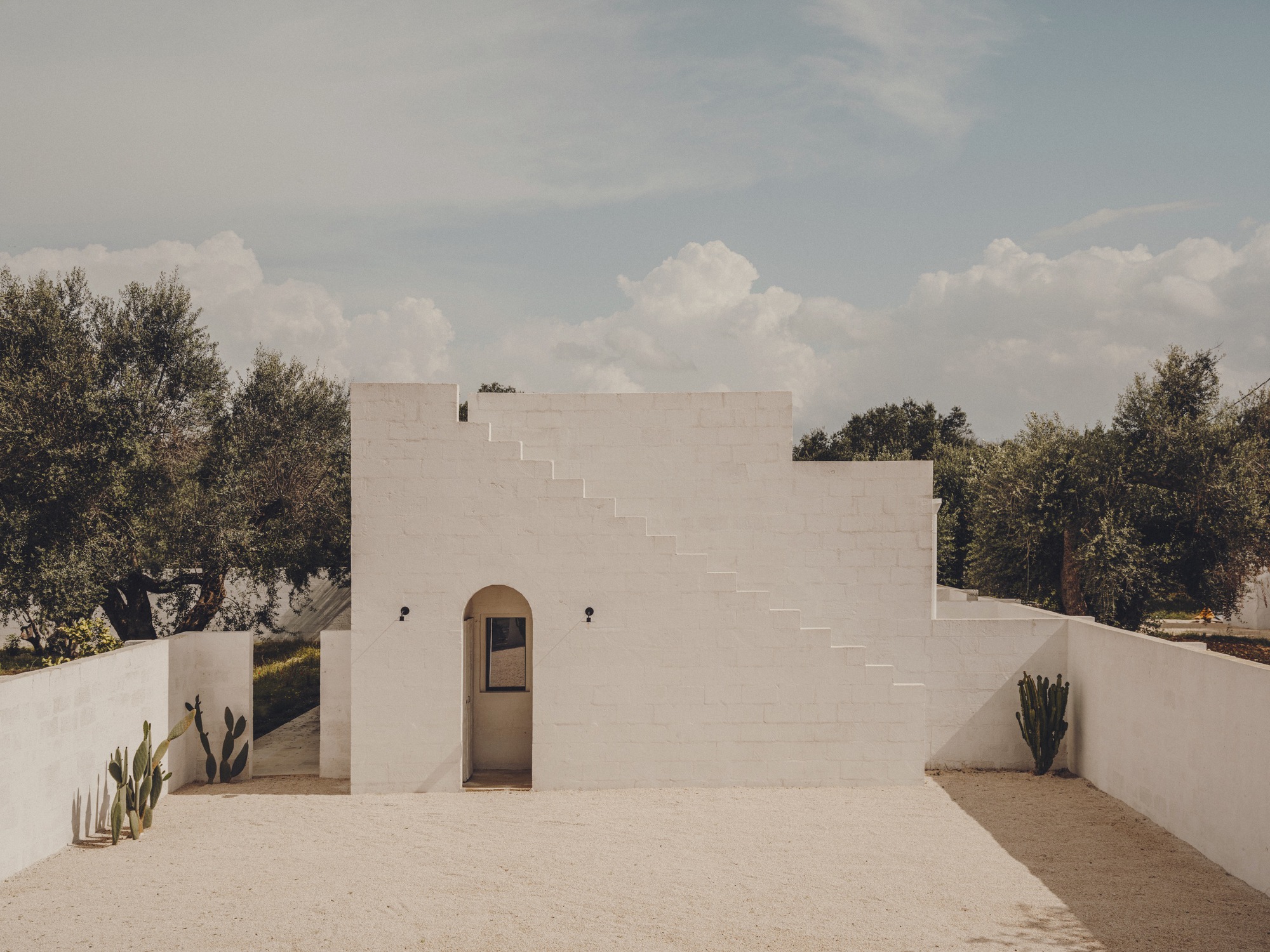 White facade with central arched doorway and stepped parapet under a cloudy sky