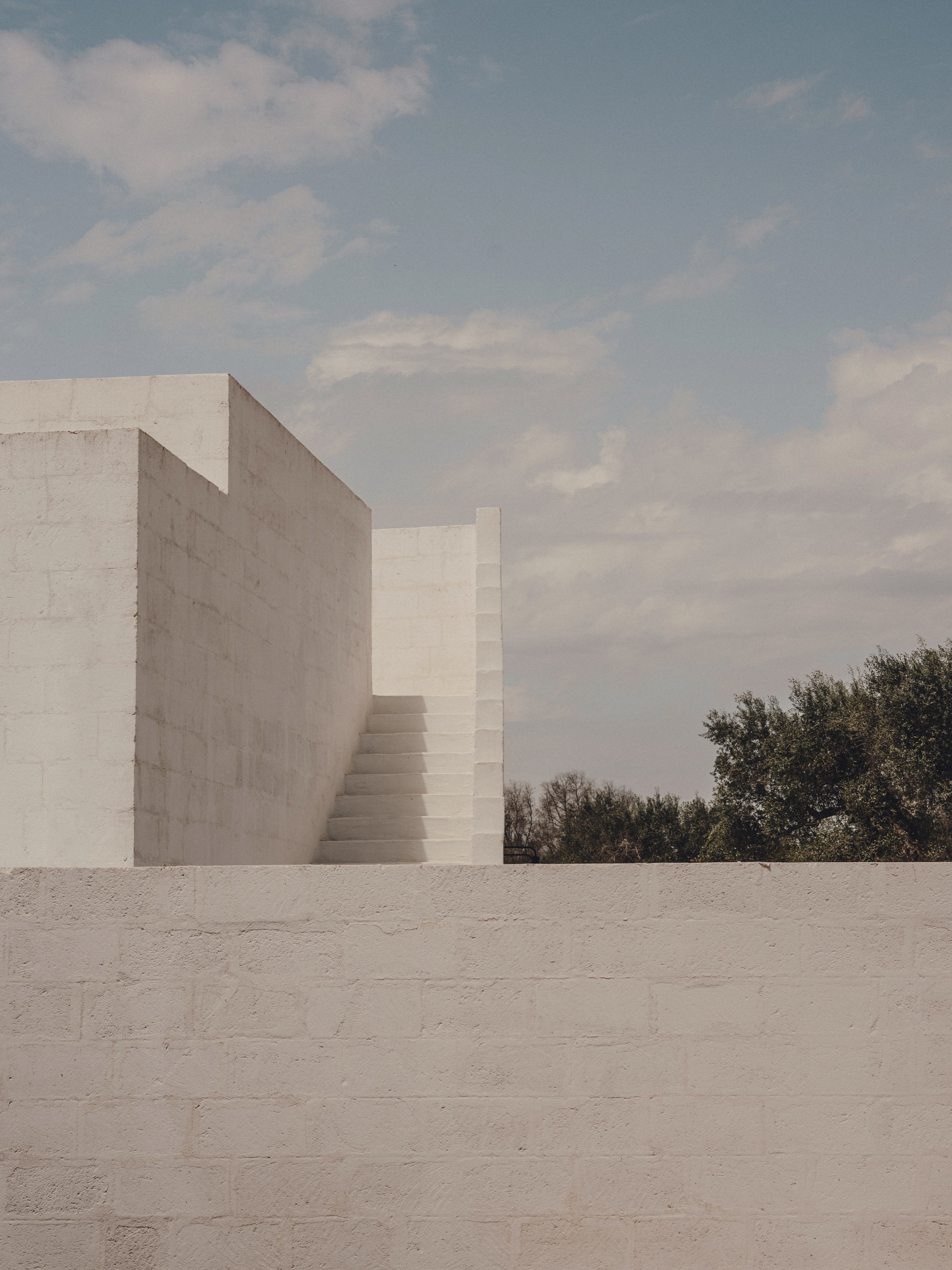White concrete staircase ascending between two angular walls against a cloudy sky
