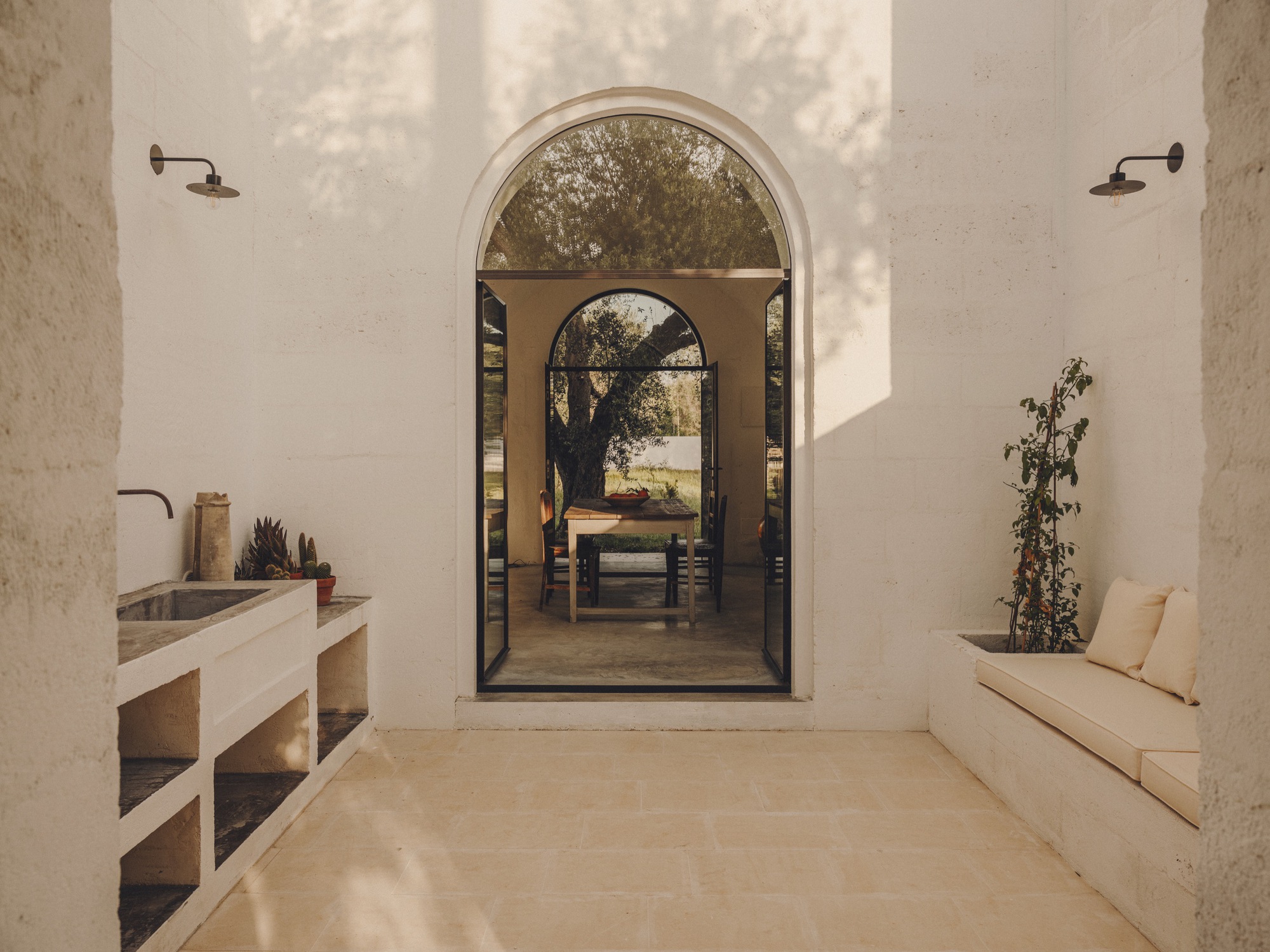 Covered terrace with built-in bench and sink looking through arched opening to dining area and tree