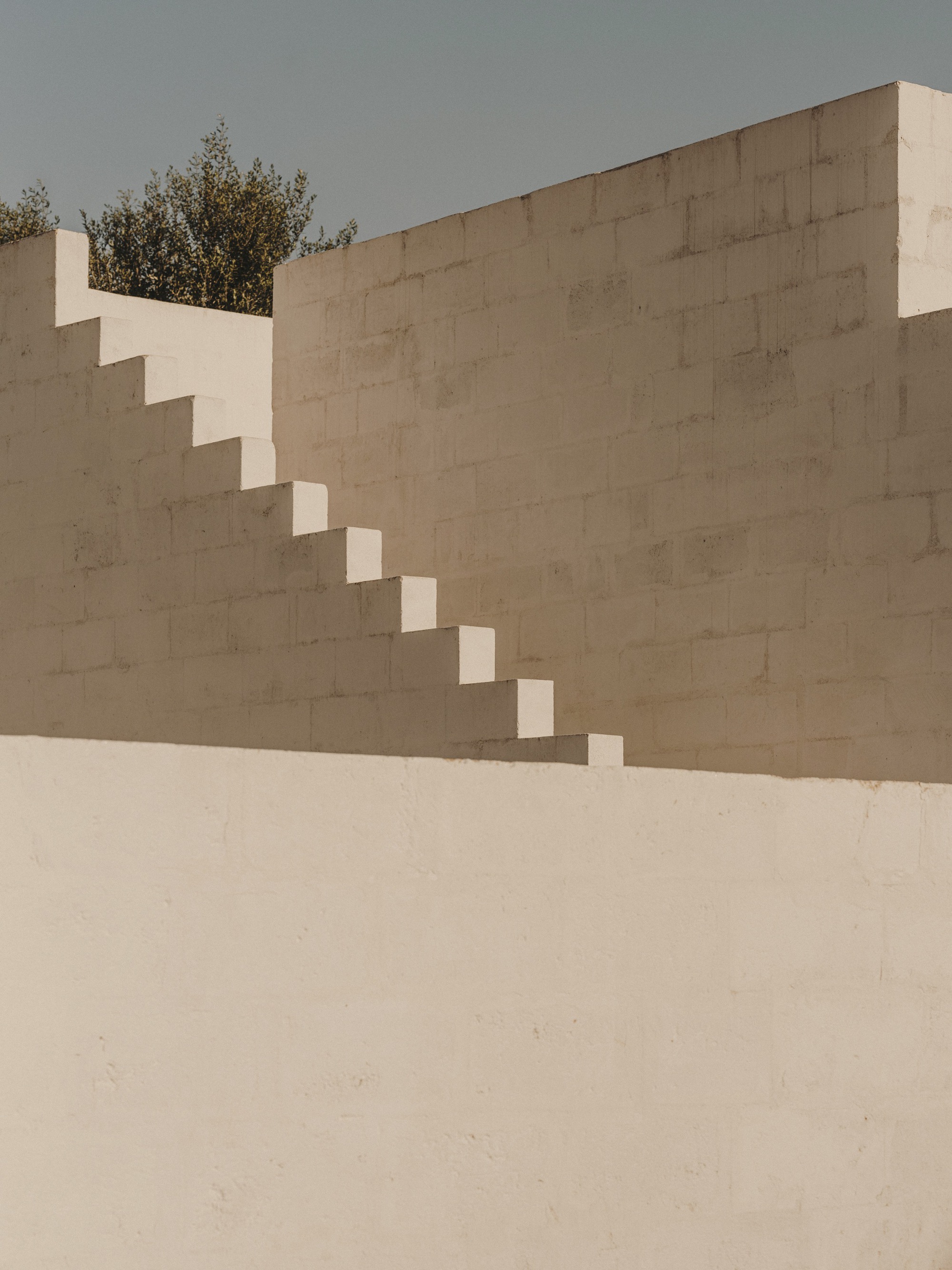 Cantilevered staircase ascending rendered wall in open courtyard beneath an overcast sky
