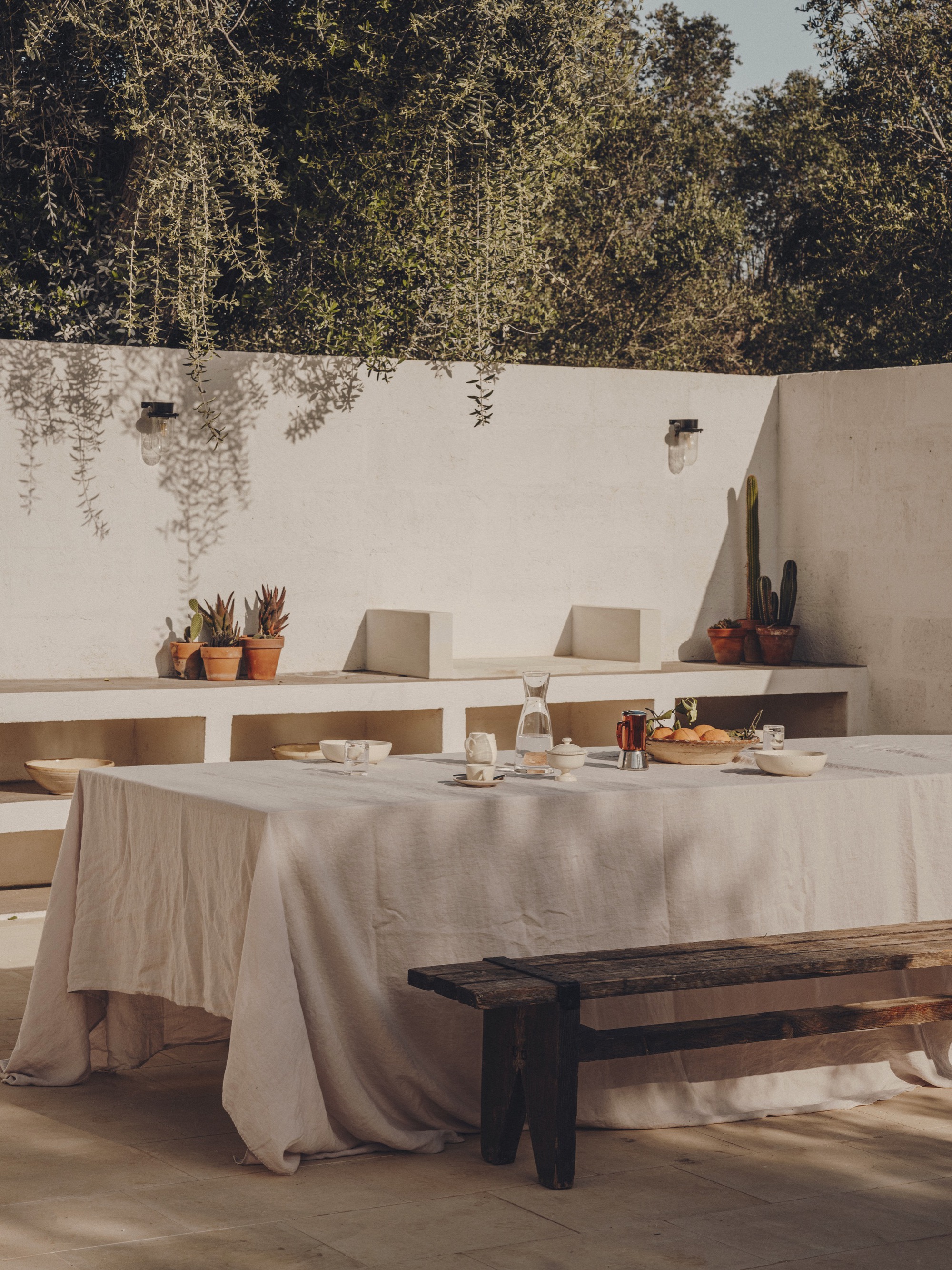Outdoor dining table set with linen cloth beneath built-in bench seating and potted succulents