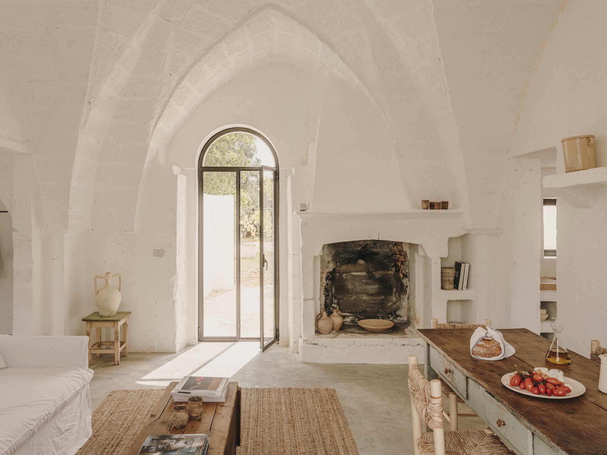 Vaulted living space with arched doorway, stone fireplace surround, and timber dining table under soft daylight