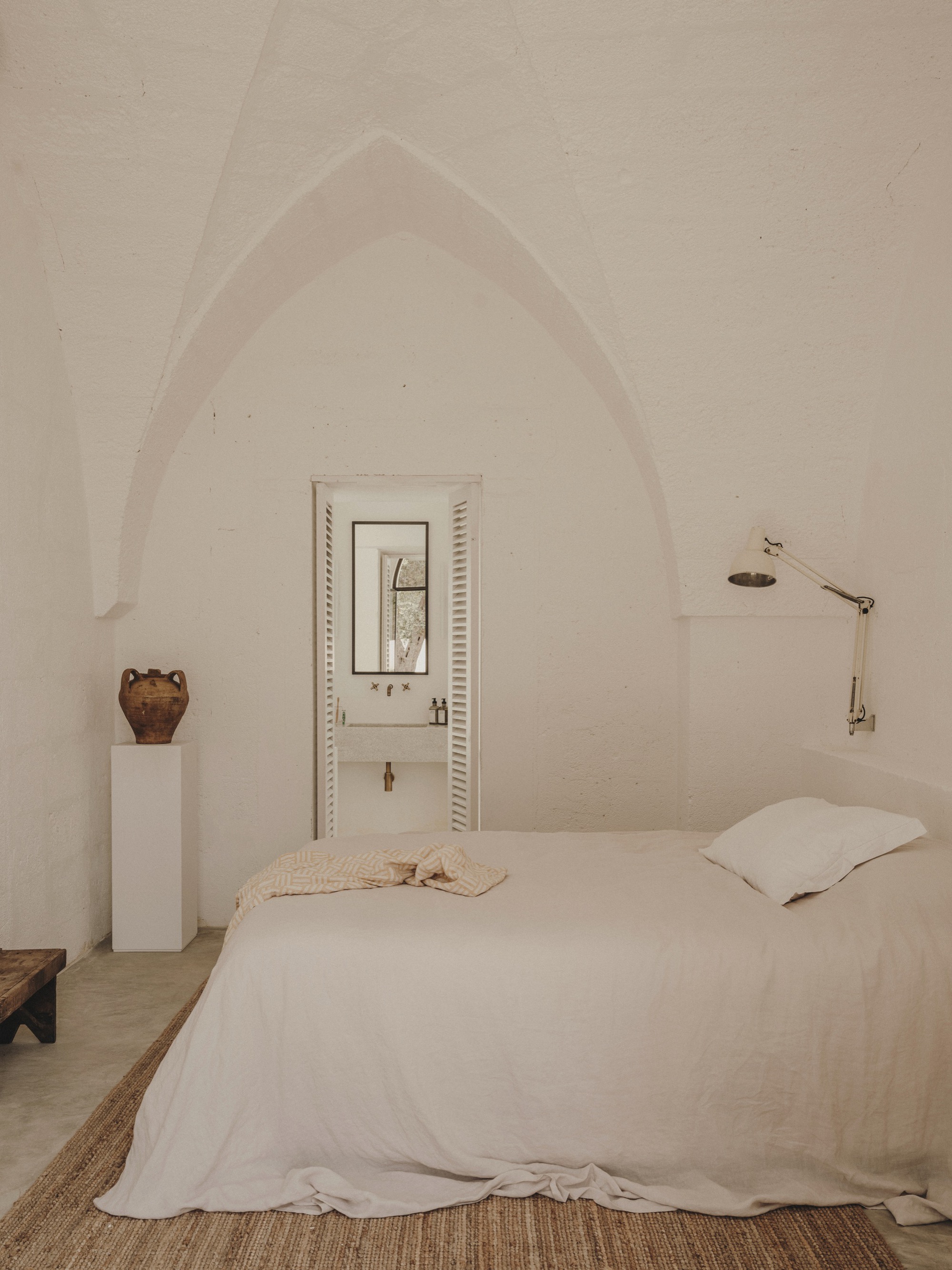 Bedroom with pointed arch vault framing doorway with louvered shutters and polished concrete floor