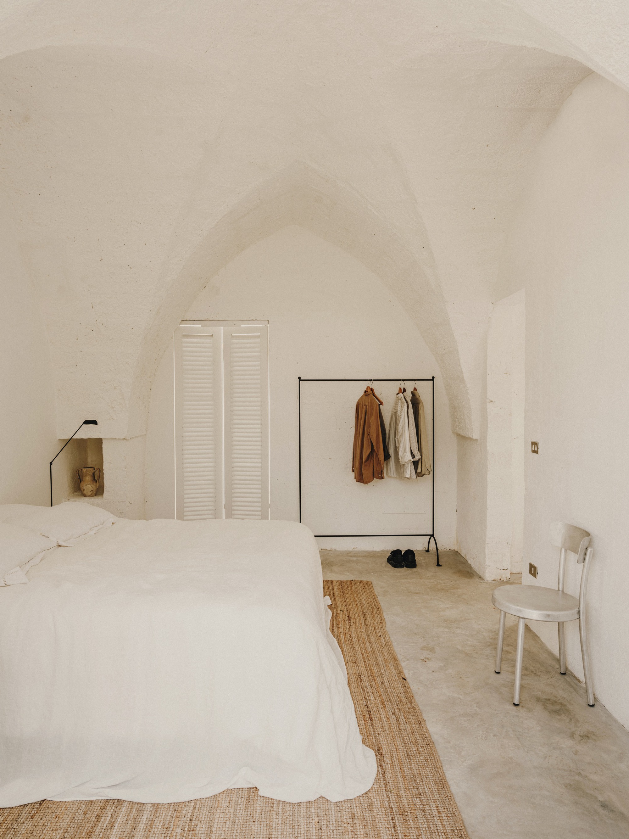 Bedroom with vaulted plaster ceiling, white louvered doors and metal clothing rack under soft daylight