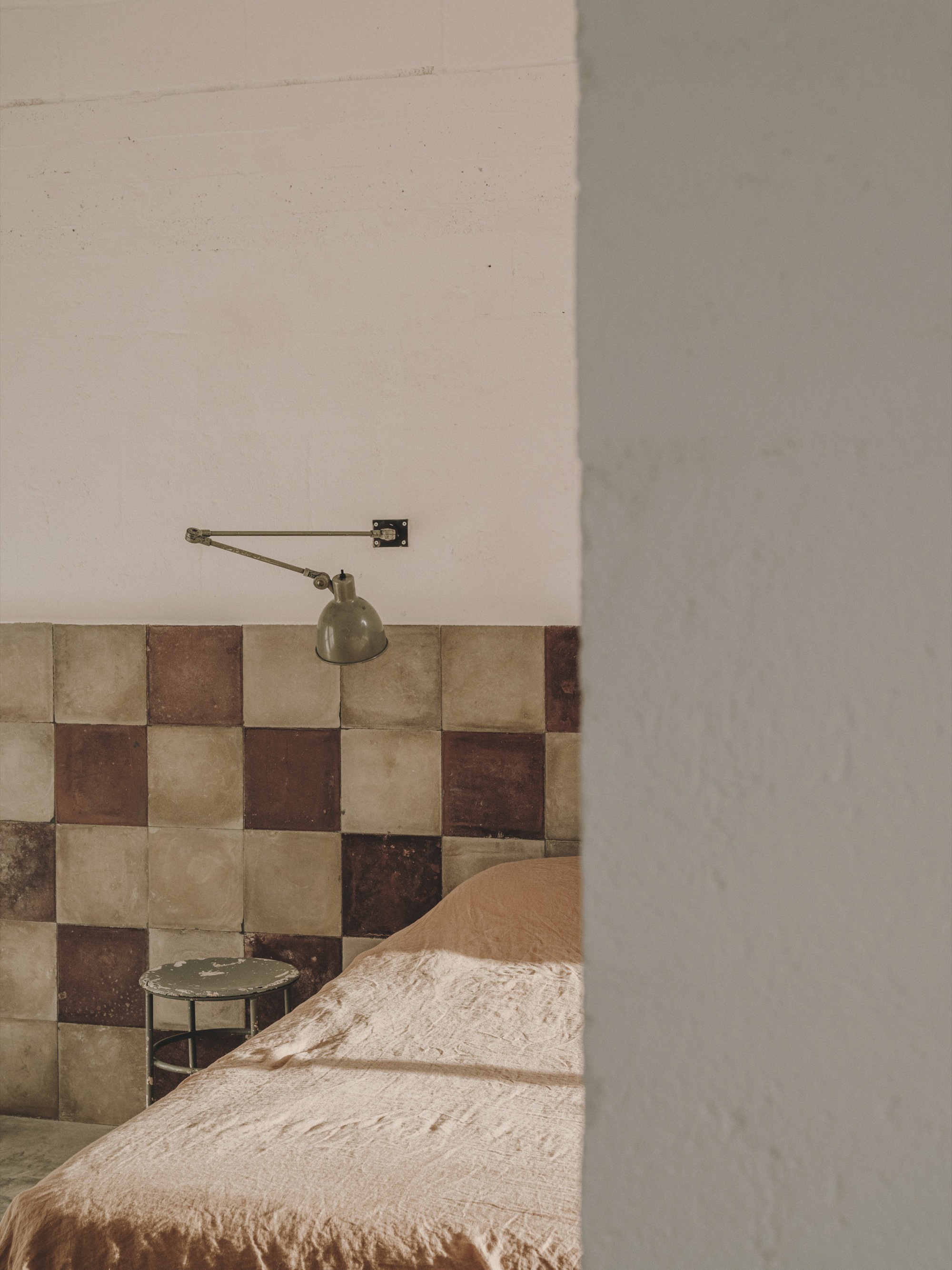 Partial view of chequered tile headboard with wall-mounted brass lamp beside plastered column