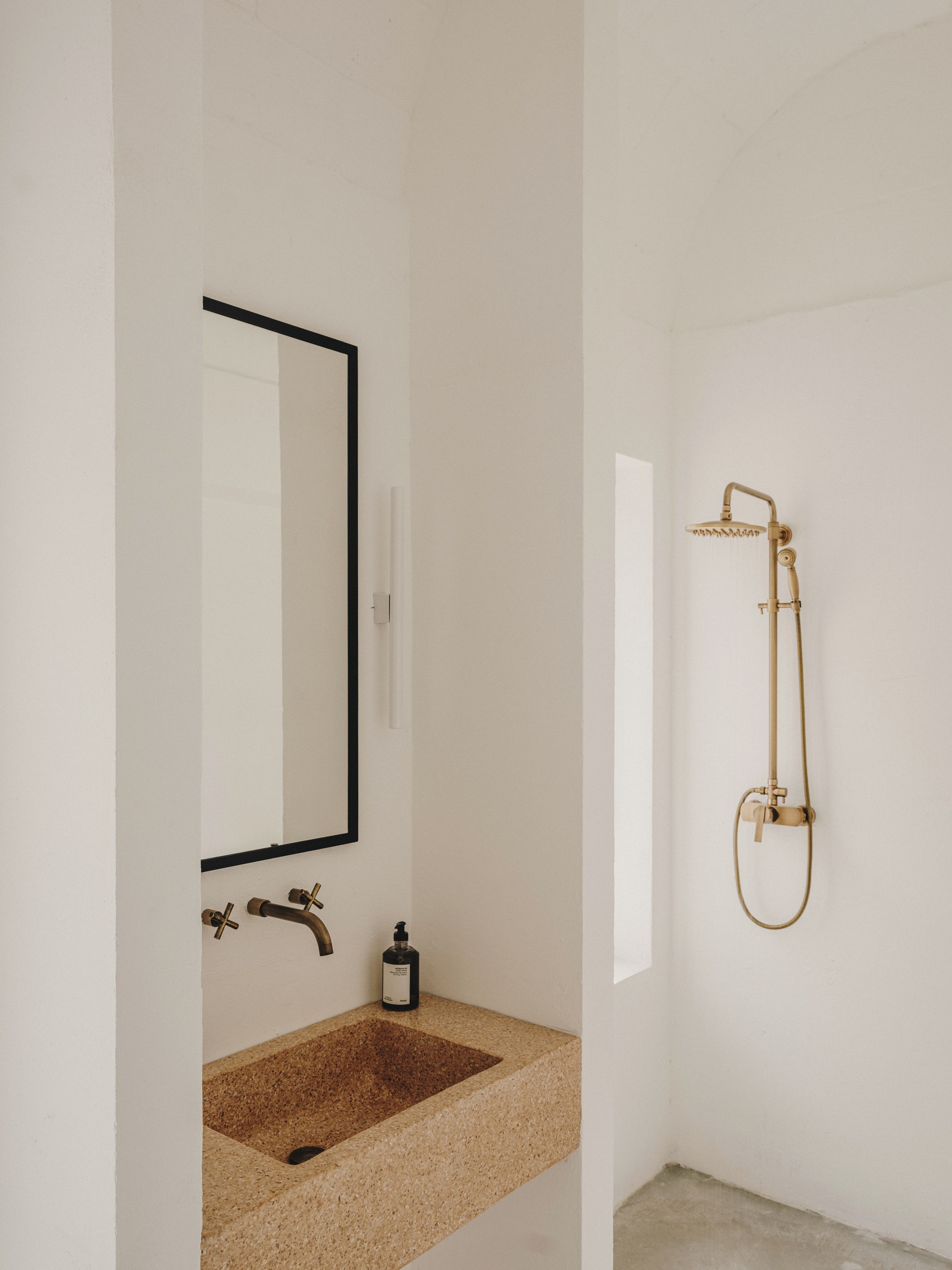 Bathroom with terrazzo sink, black-framed mirror and brass shower fixtures against white walls