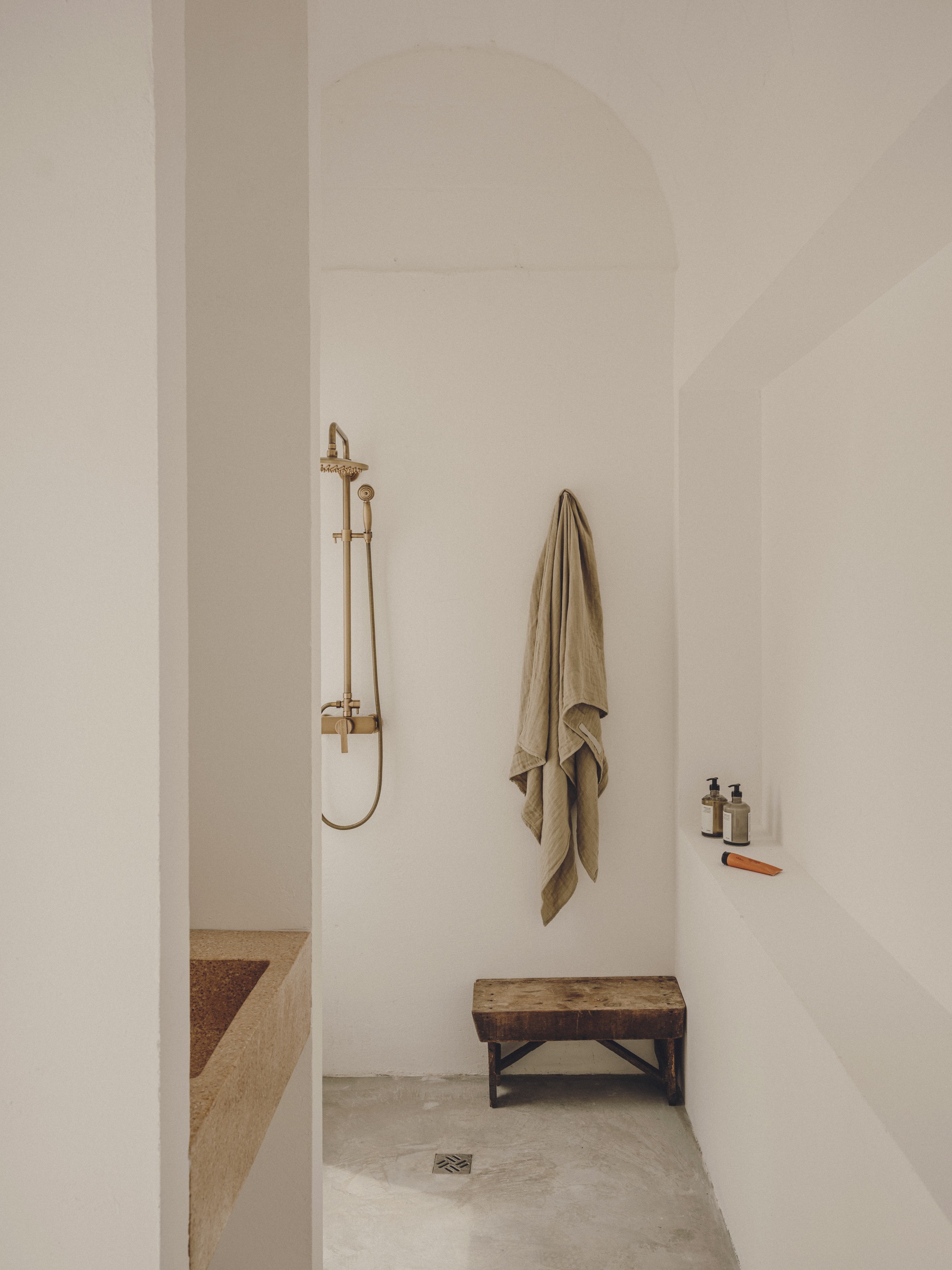 Shower alcove with brass fixtures, arched ceiling and timber bench on concrete floor