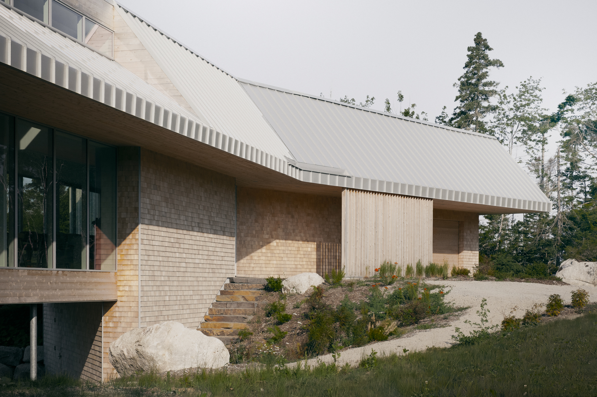 Exterior facade combining pale brick, vertical wood cladding, and a sweeping metal roof