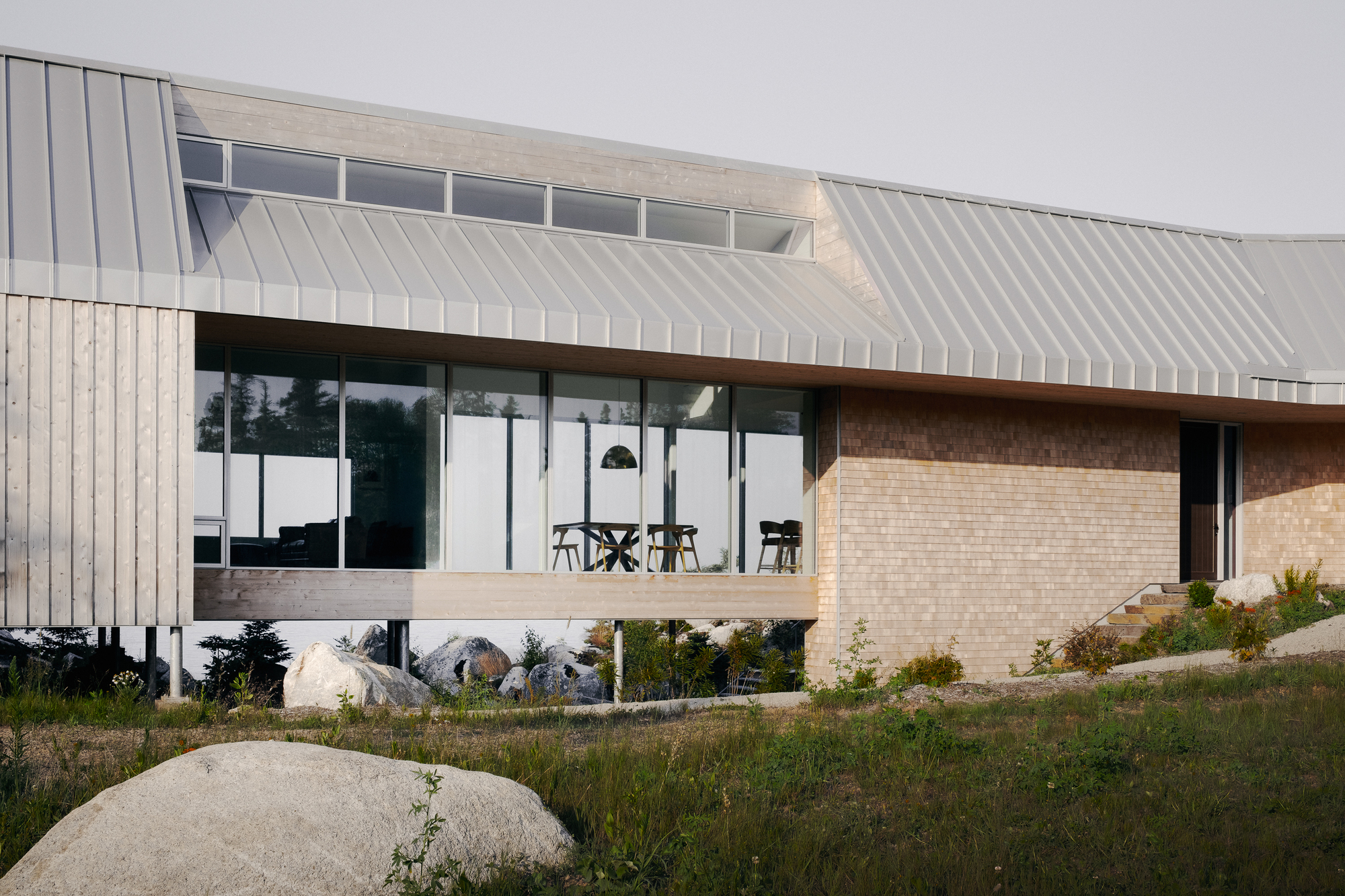Elevated glazed living area with standing seam metal roof above a cream brick plinth in dry grasses
