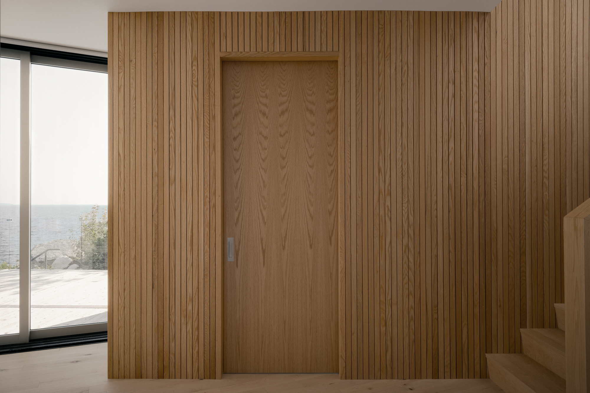Vertical timber slat wall concealing recessed door with view to terrace and sea beyond