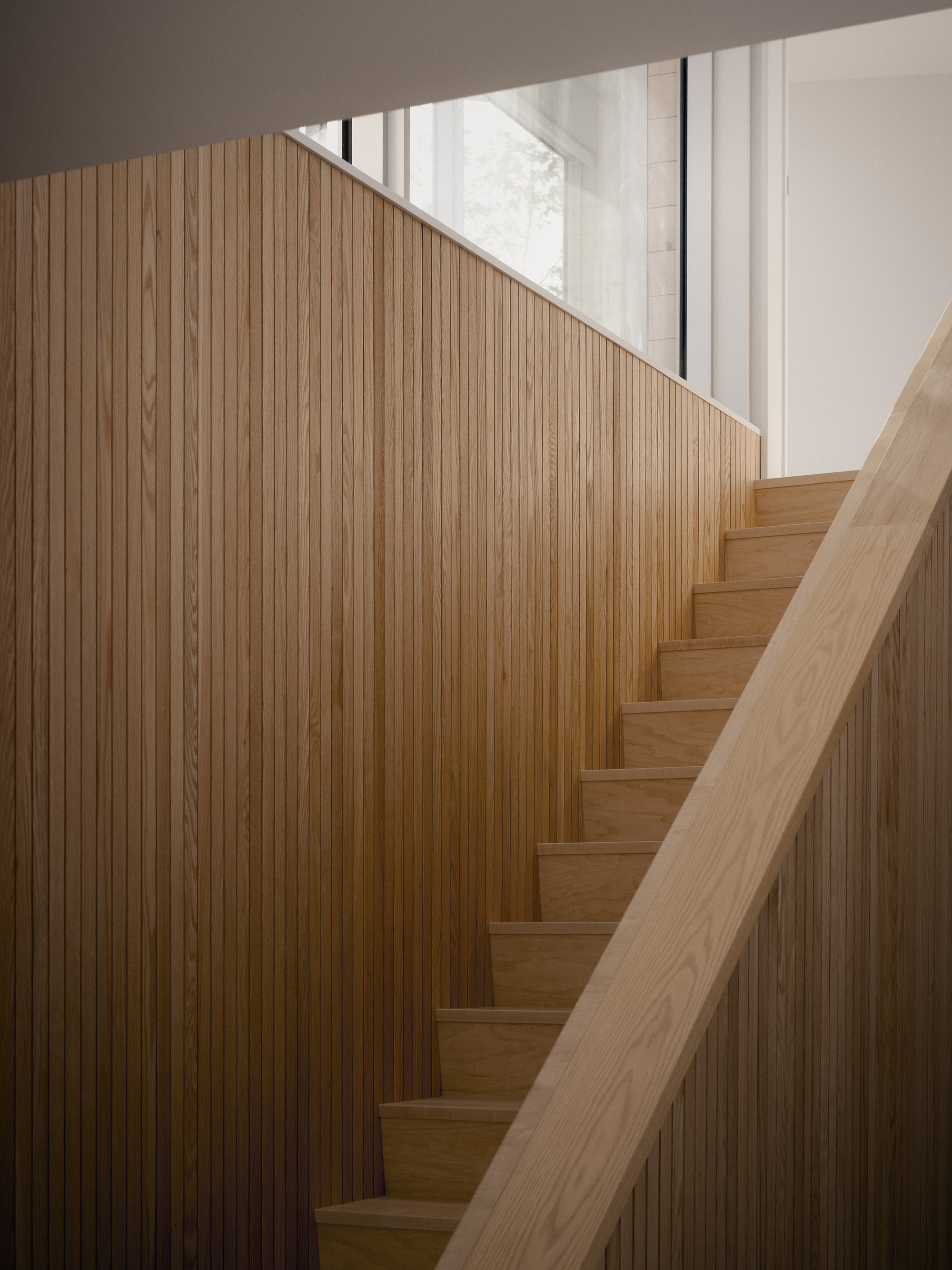 Timber staircase with vertical slat wall and integrated handrail beneath a skylight