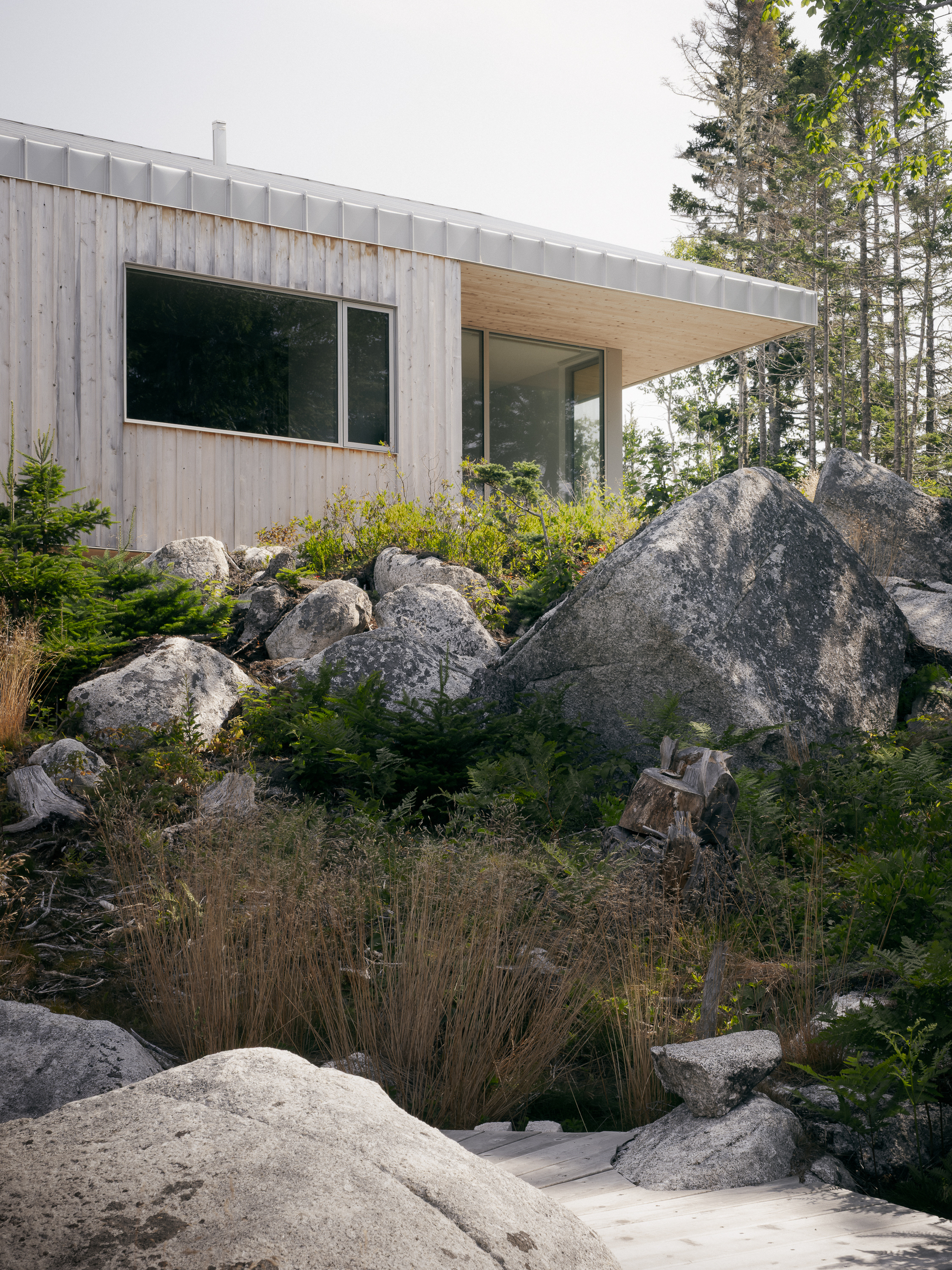 Timber-clad volume with metal seam roof nestled among granite outcrops and low plantings