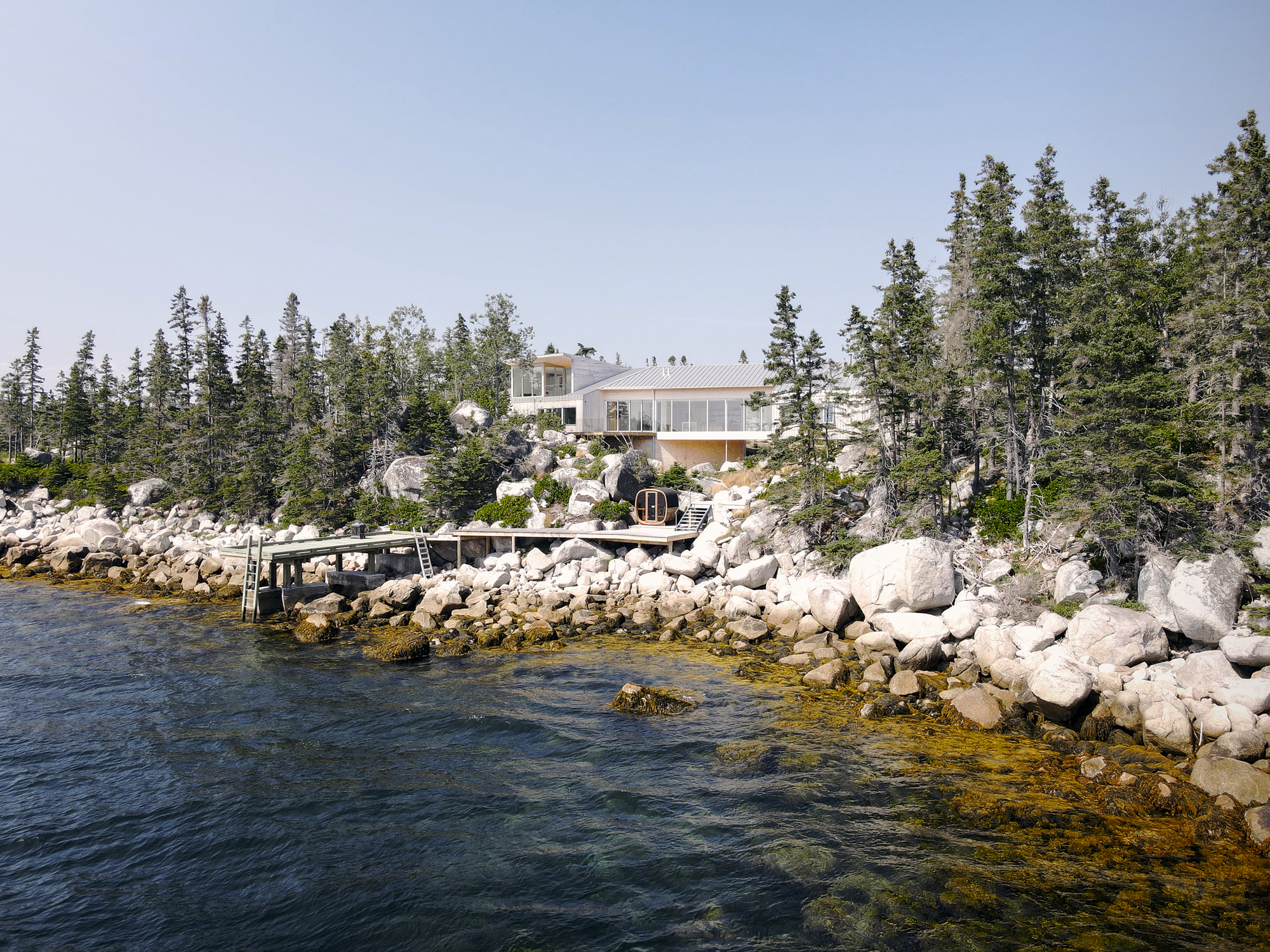 Waterfront house on a rocky outcrop with evergreen forest and small dock extending into calm water