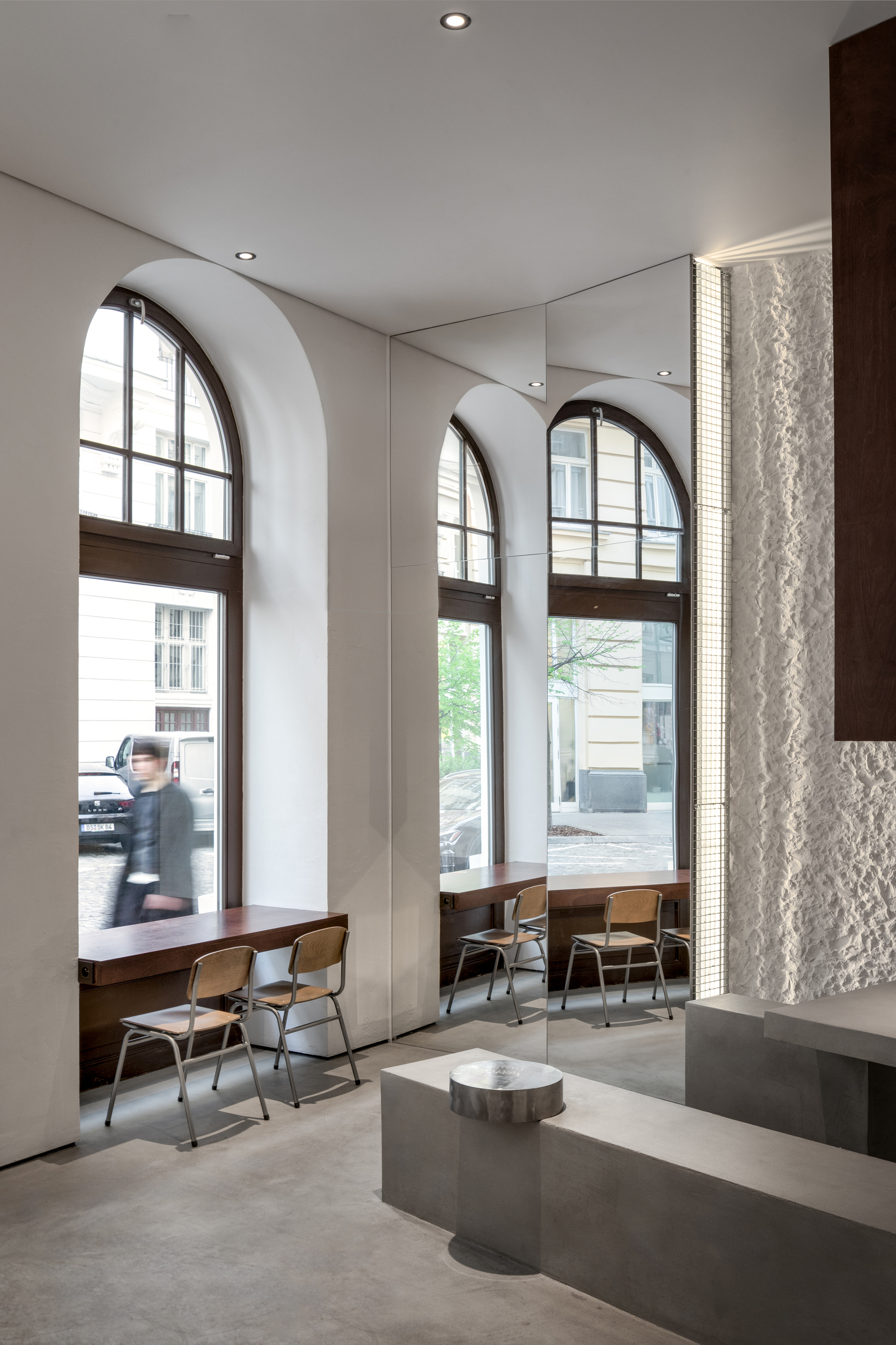 Tall arched windows with deep reveals overlooking the street, a figure passing by the seating below