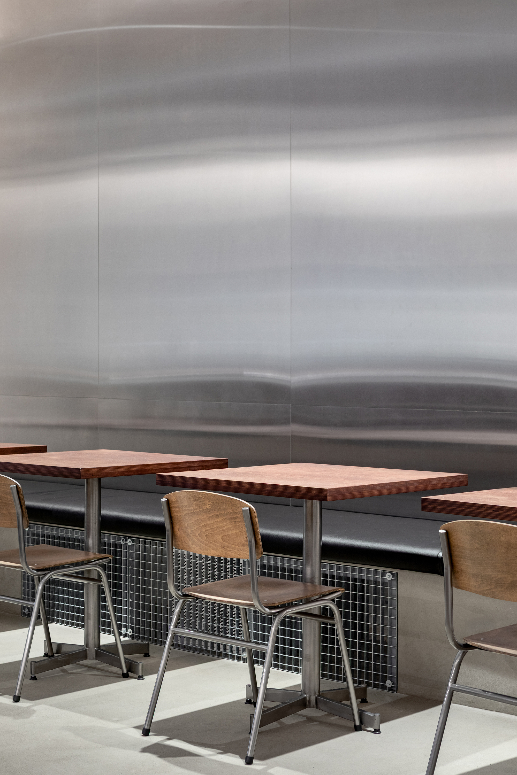 Cafe seating with wood tables and metal chairs against a brushed steel landscape mural