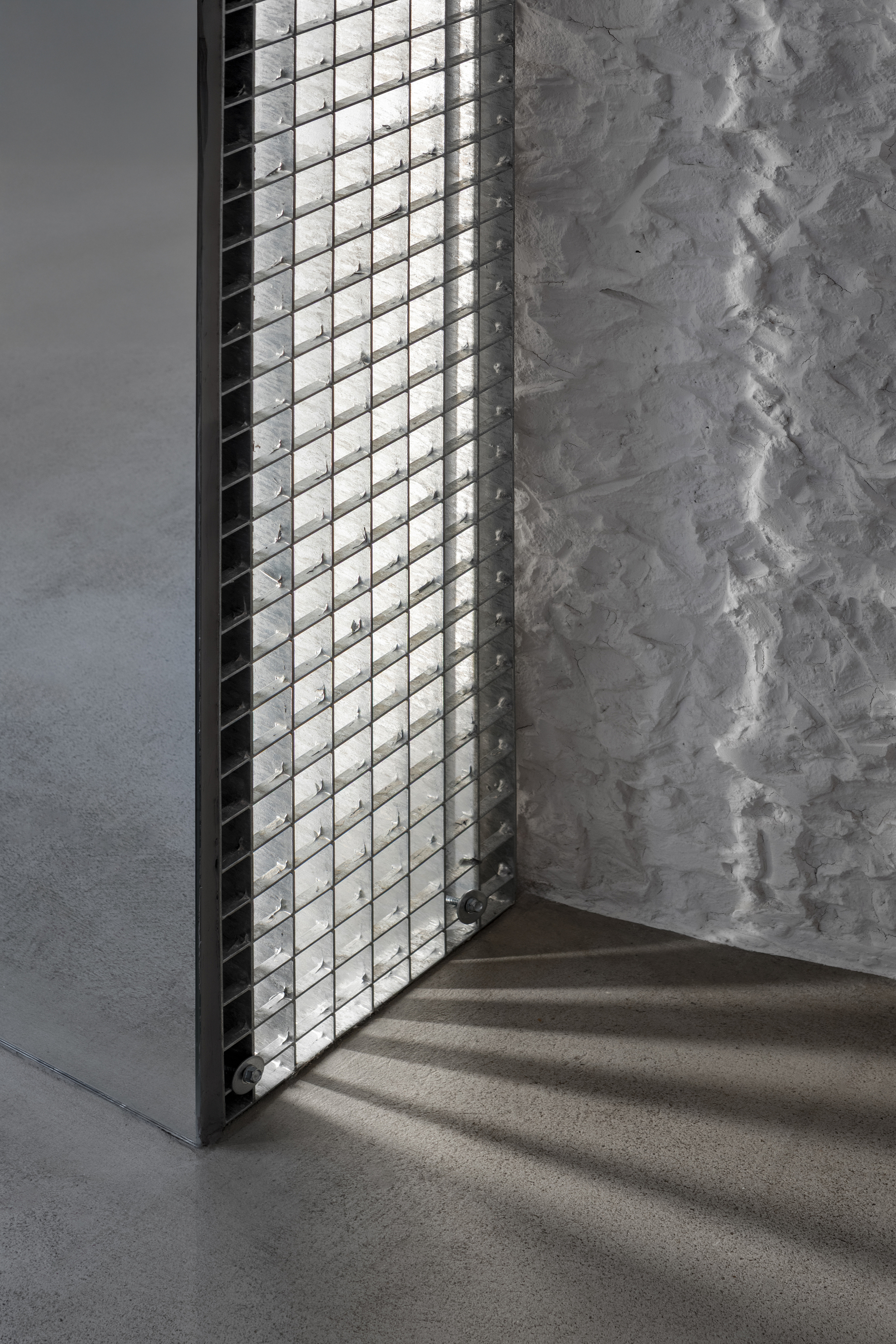 Glass block window casting diamond shadows on concrete floor beside a weathered plaster wall